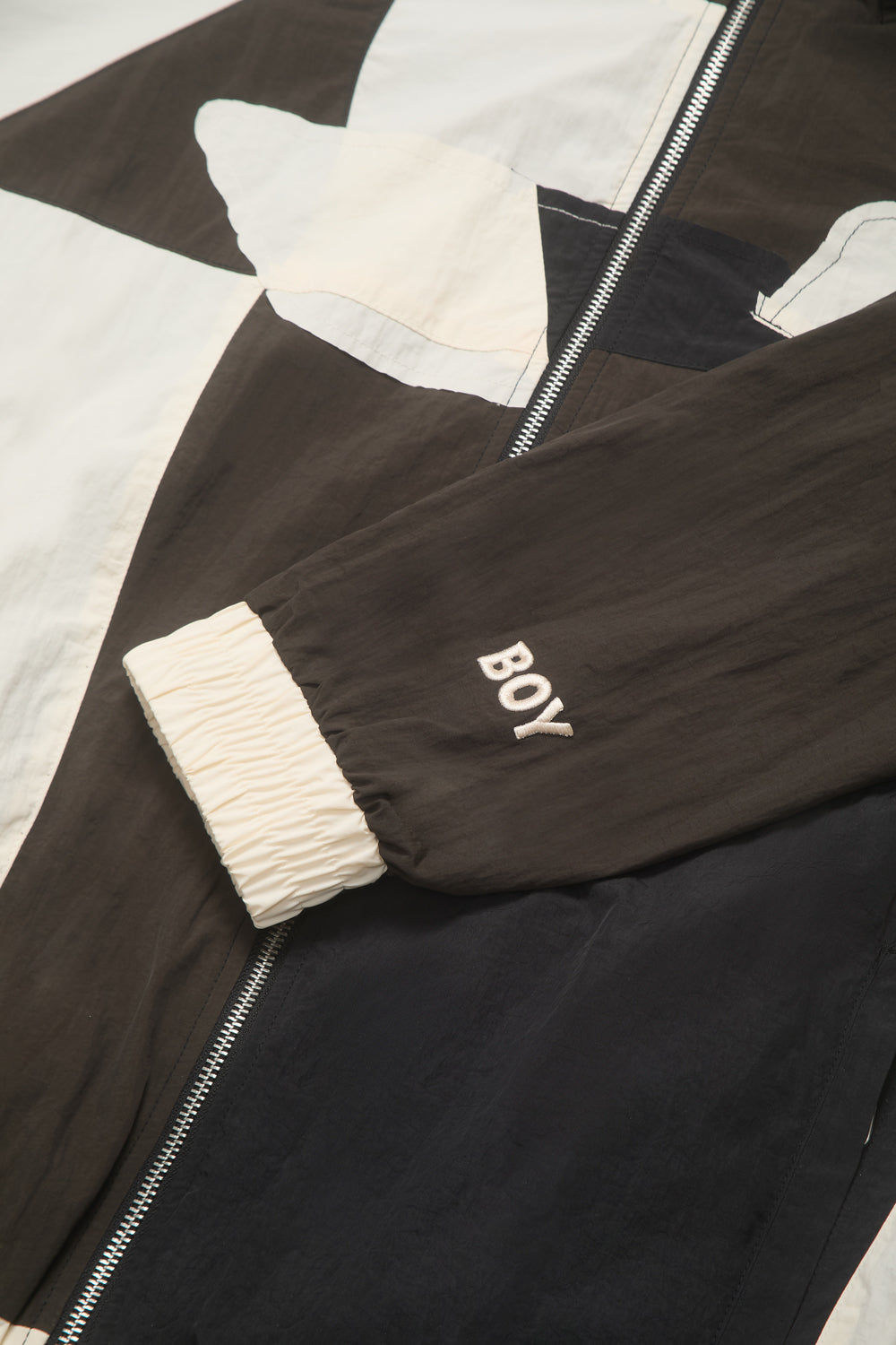 Black jacket with white cuffs and 'BOY' embroidery on a patterned surface