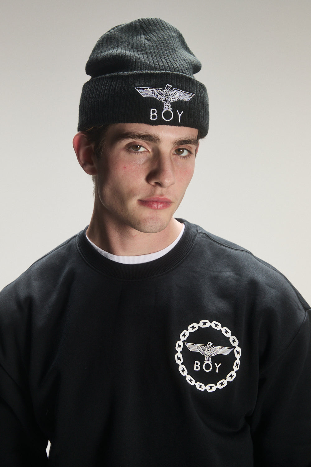 Person wearing a black beanie and sweatshirt with 'BOY' London logo on a plain background