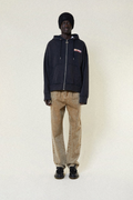 Person wearing a dark hoodie with a BOY London logo, beige pants, and black shoes on a white background