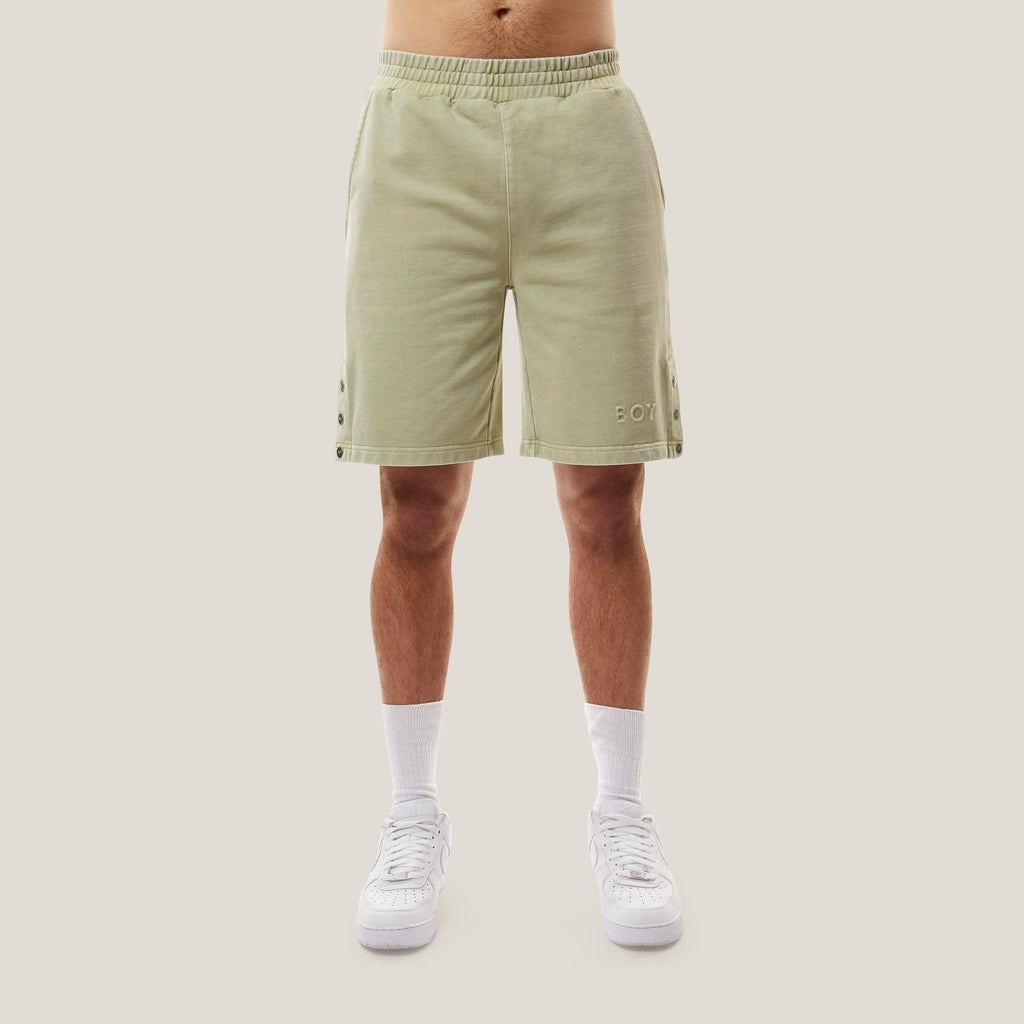 Model wearing Green BOY London shorts with button details on a white background