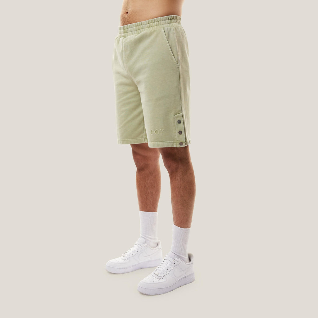 Model wearing Green BOY London shorts with button details on a white background