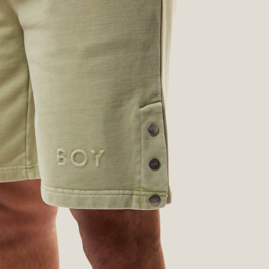 Model wearing Green BOY London shorts with button details on a white background