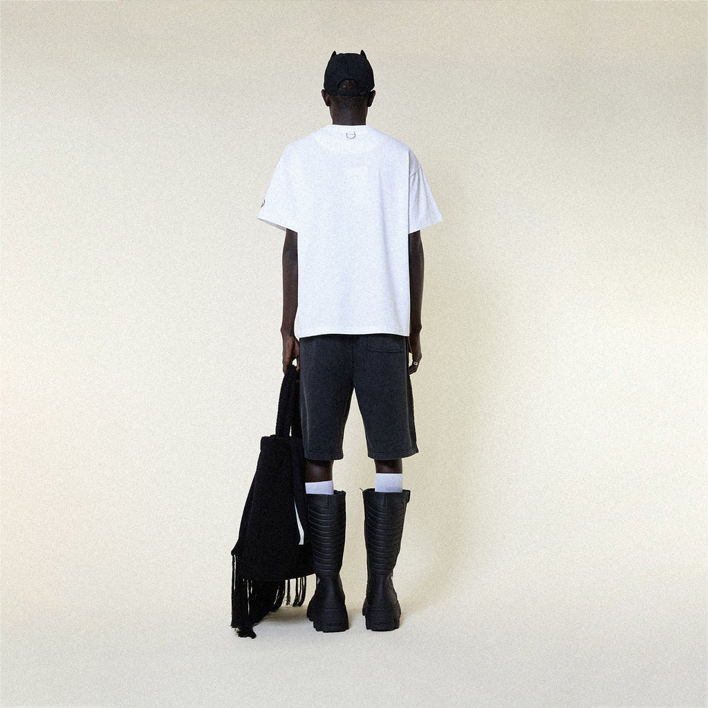 Person wearing a BOY LONDON white t-shirt with 'BOY RACER' text, black shorts, and black boots on a plain background