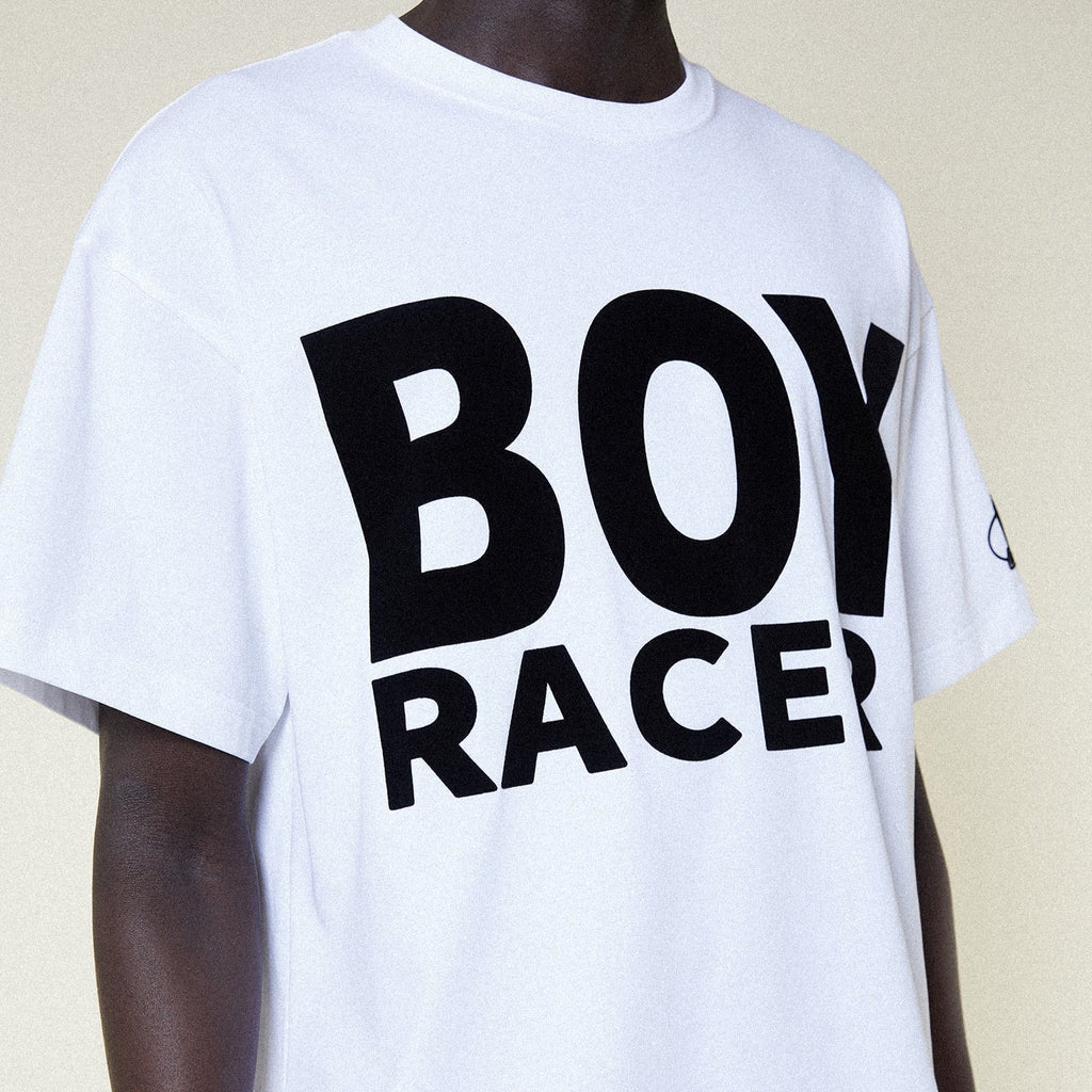 Person wearing a BOY LONDON white t-shirt with 'BOY RACER' text, black shorts, and black boots on a plain background