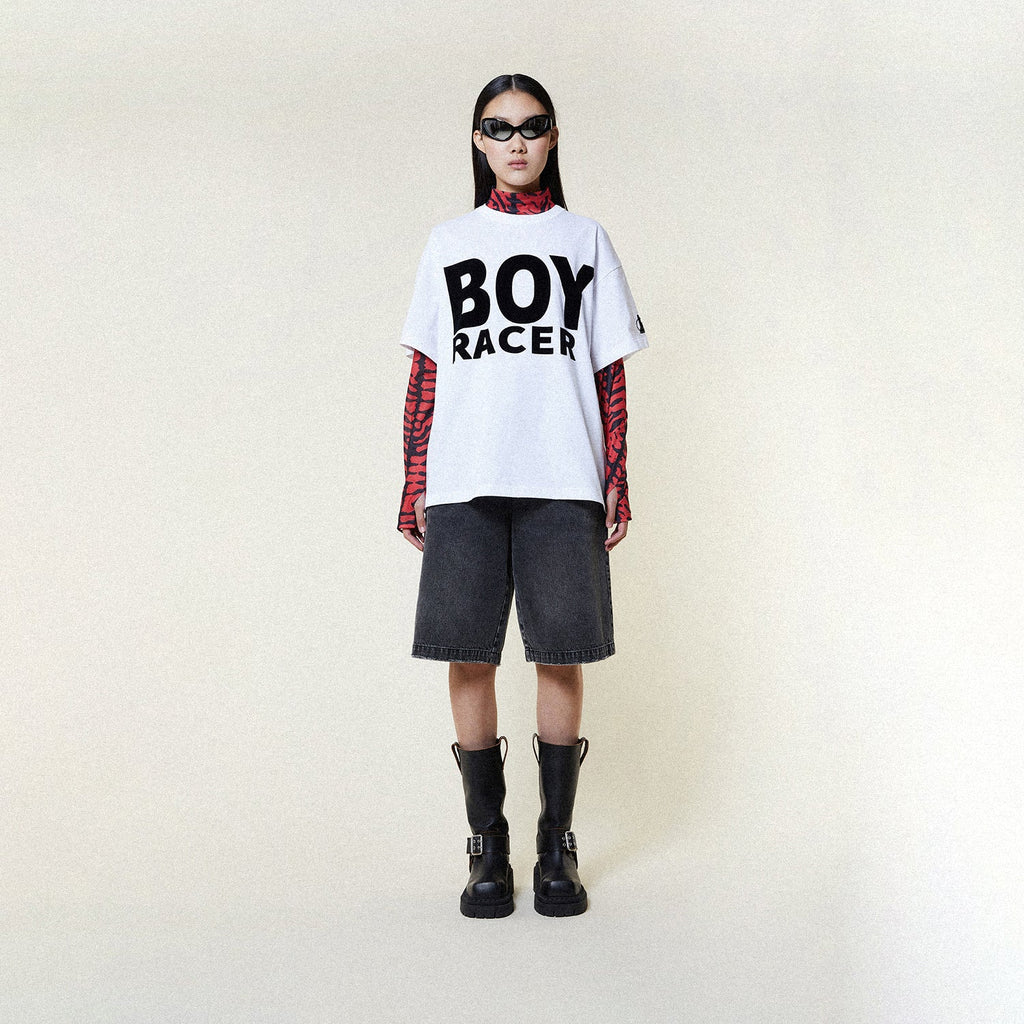 Person wearing a BOY LONDON white t-shirt with 'BOY RACER' text, black shorts, and black boots on a plain background