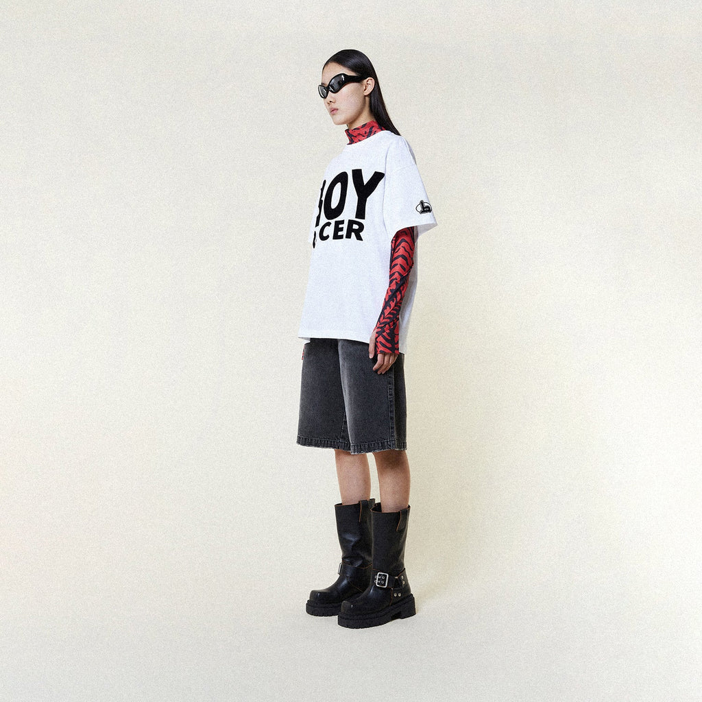 Person wearing a BOY LONDON white t-shirt with 'BOY RACER' text, black shorts, and black boots on a plain background