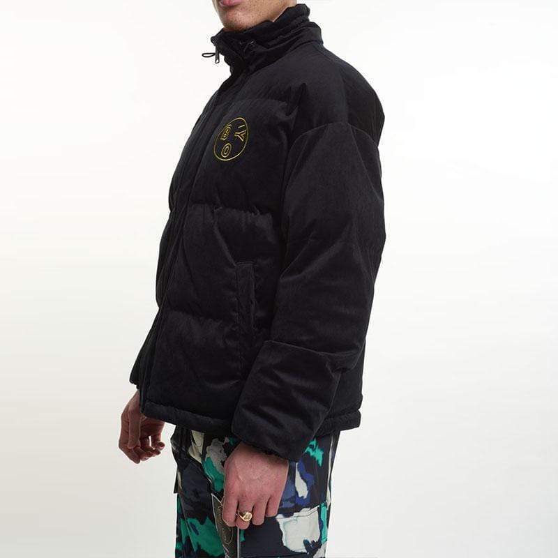 Man wearing a black BOY London jacket with a logo and colorful pants on a white background