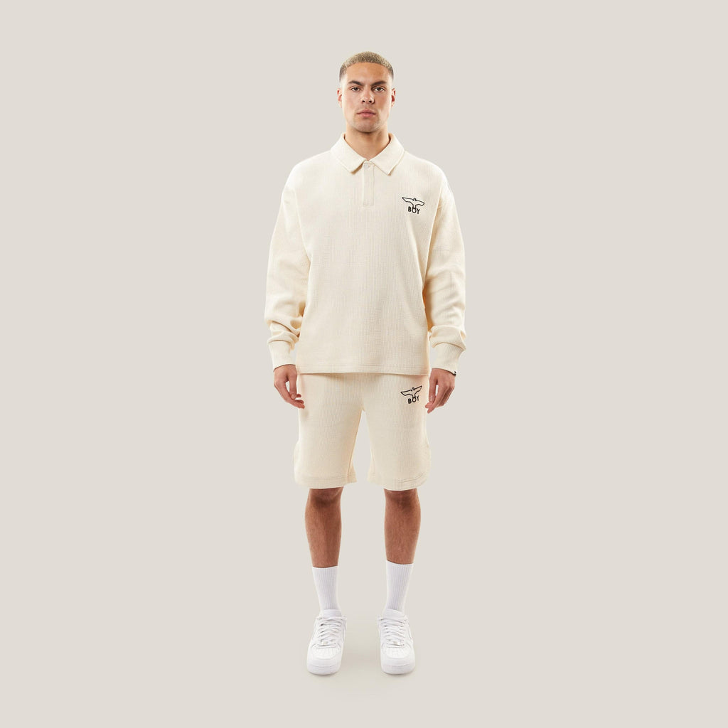 Model wearing BOY London Beige shorts with a logo on a white background