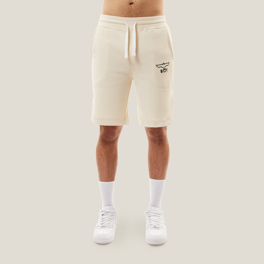 Model wearing BOY London Beige shorts with a logo on a white background