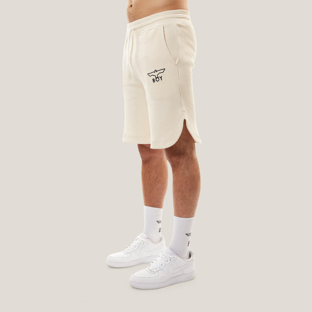 Model wearing BOY London Beige shorts with a logo on a white background