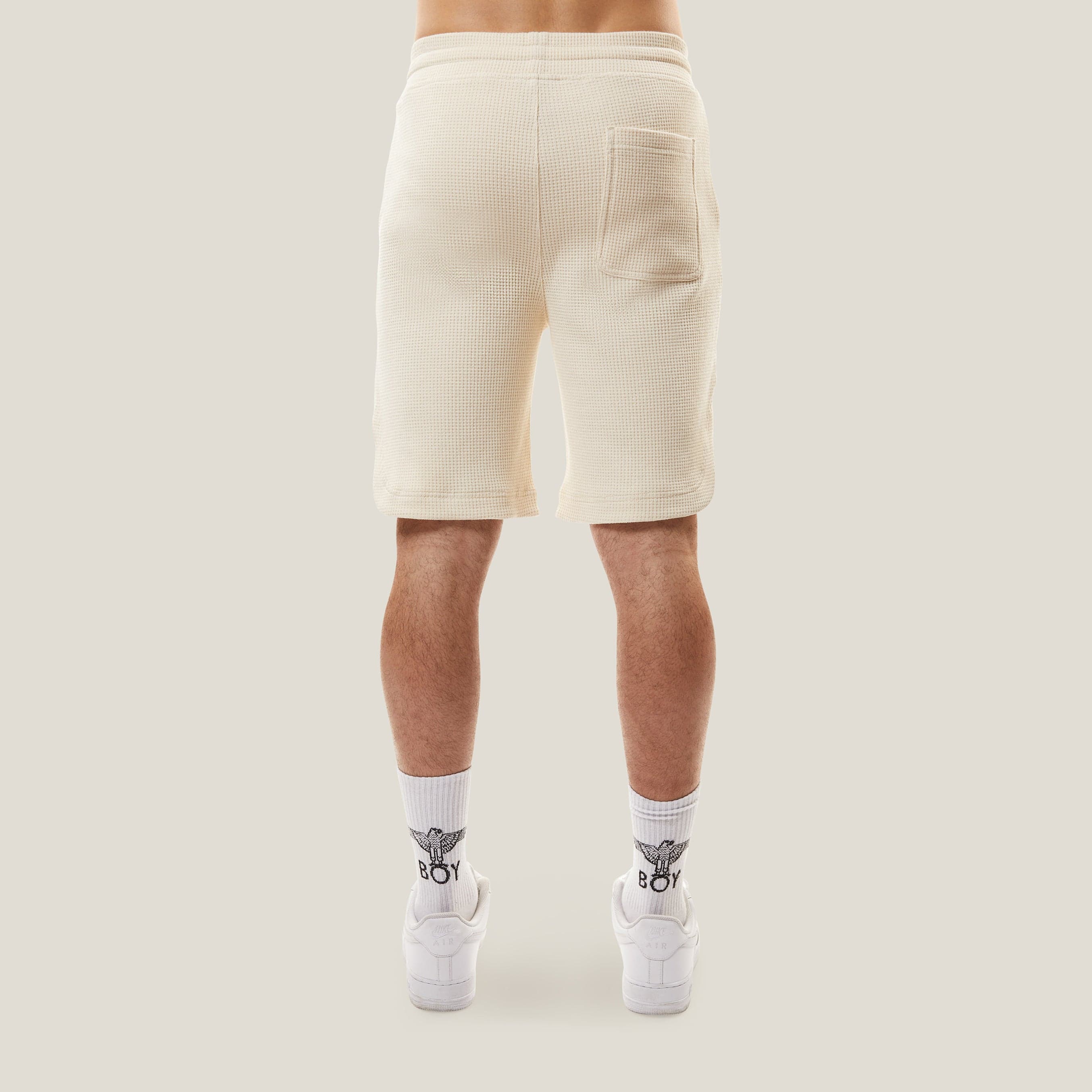Model wearing BOY London Beige shorts with a logo on a white background