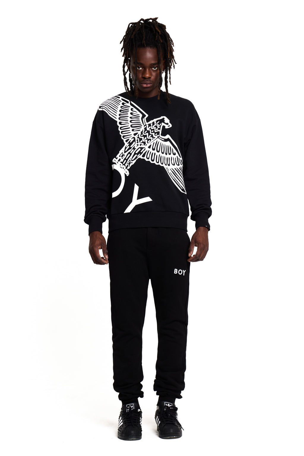 Person wearing a black BOY London sweatshirt with an eagle design and black pants with 'BOY' branding on a white background