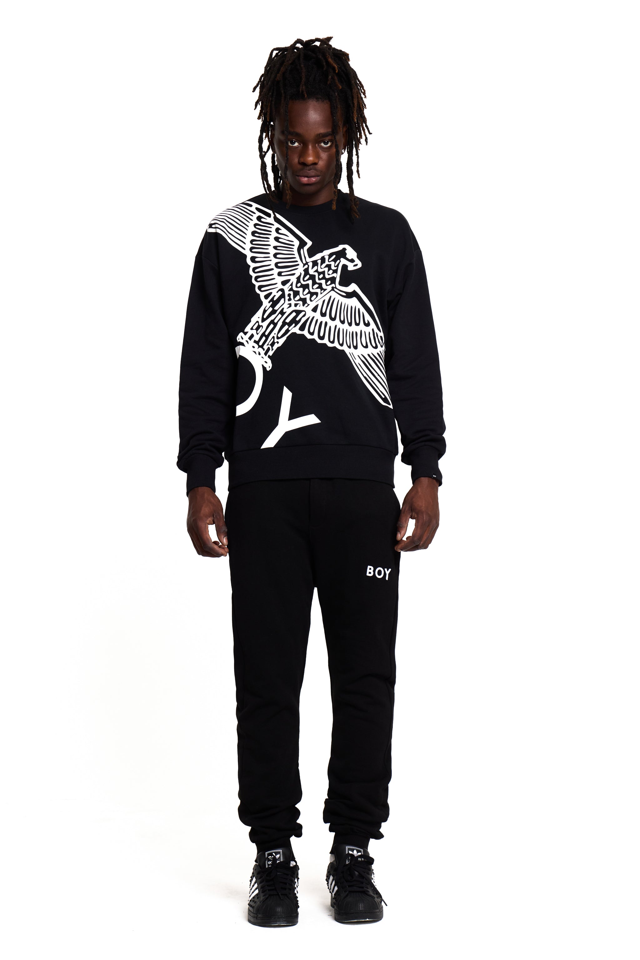 Person wearing a black BOY London sweatshirt with an eagle design and black pants with 'BOY' branding on a white background