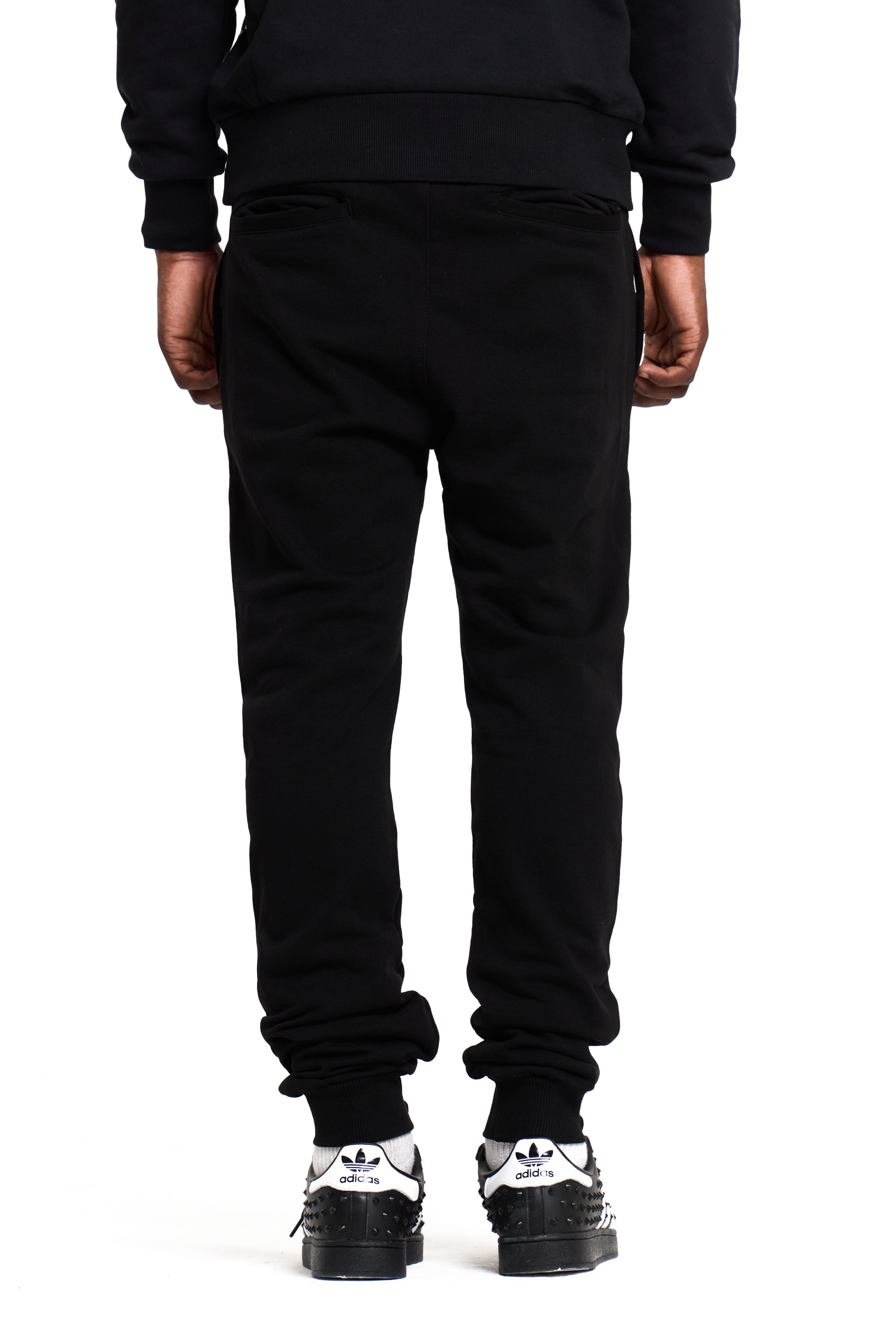 Person wearing black BOY london sweatpants and Adidas shoes on a white background
