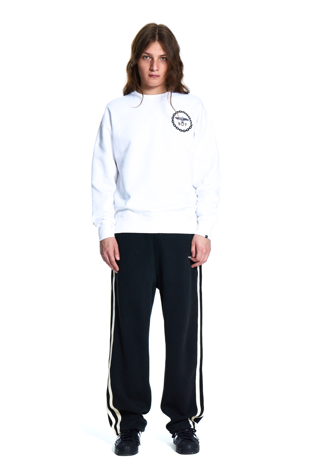 Person wearing a white Boy London hoodie and black tracksuit with white stripes on a white background