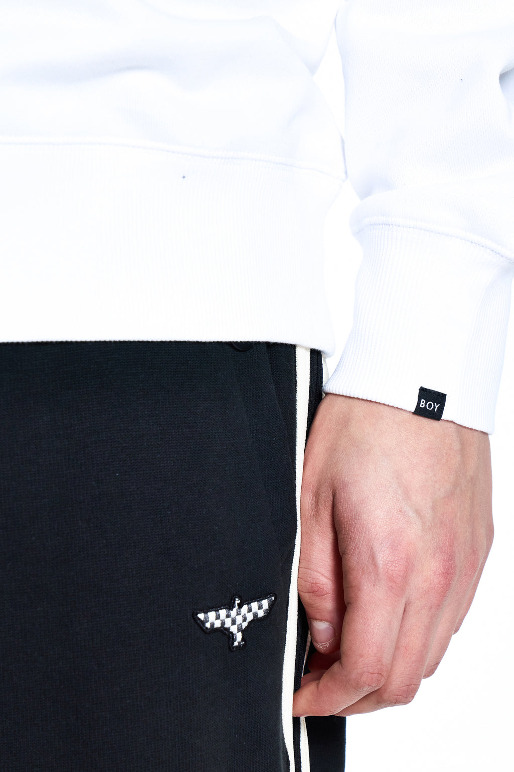 Black BOY London pants with a white logo held by a hand, wearing a white shirt with a brand label.