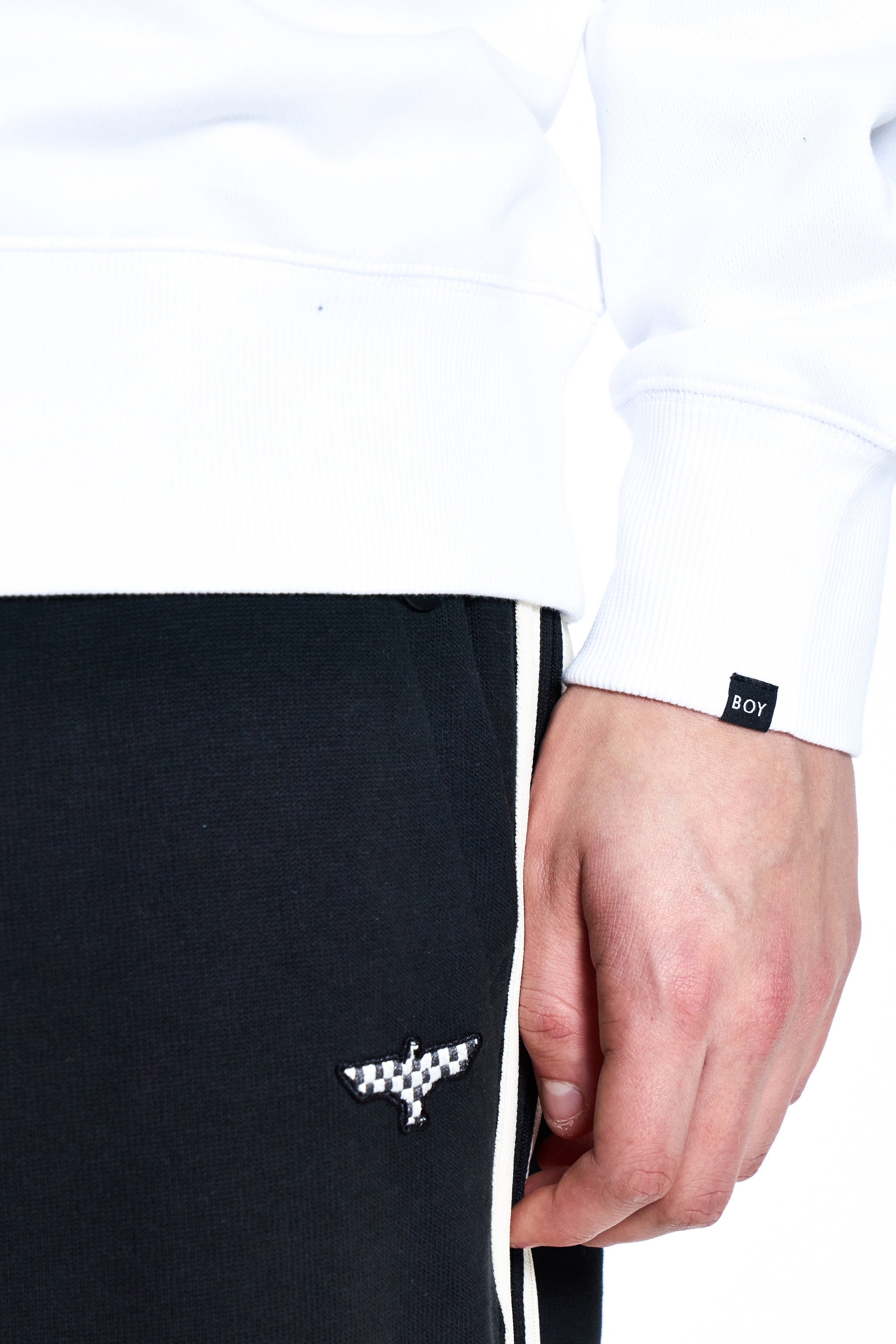 Black BOY London pants with a white logo held by a hand, wearing a white shirt with a brand label.