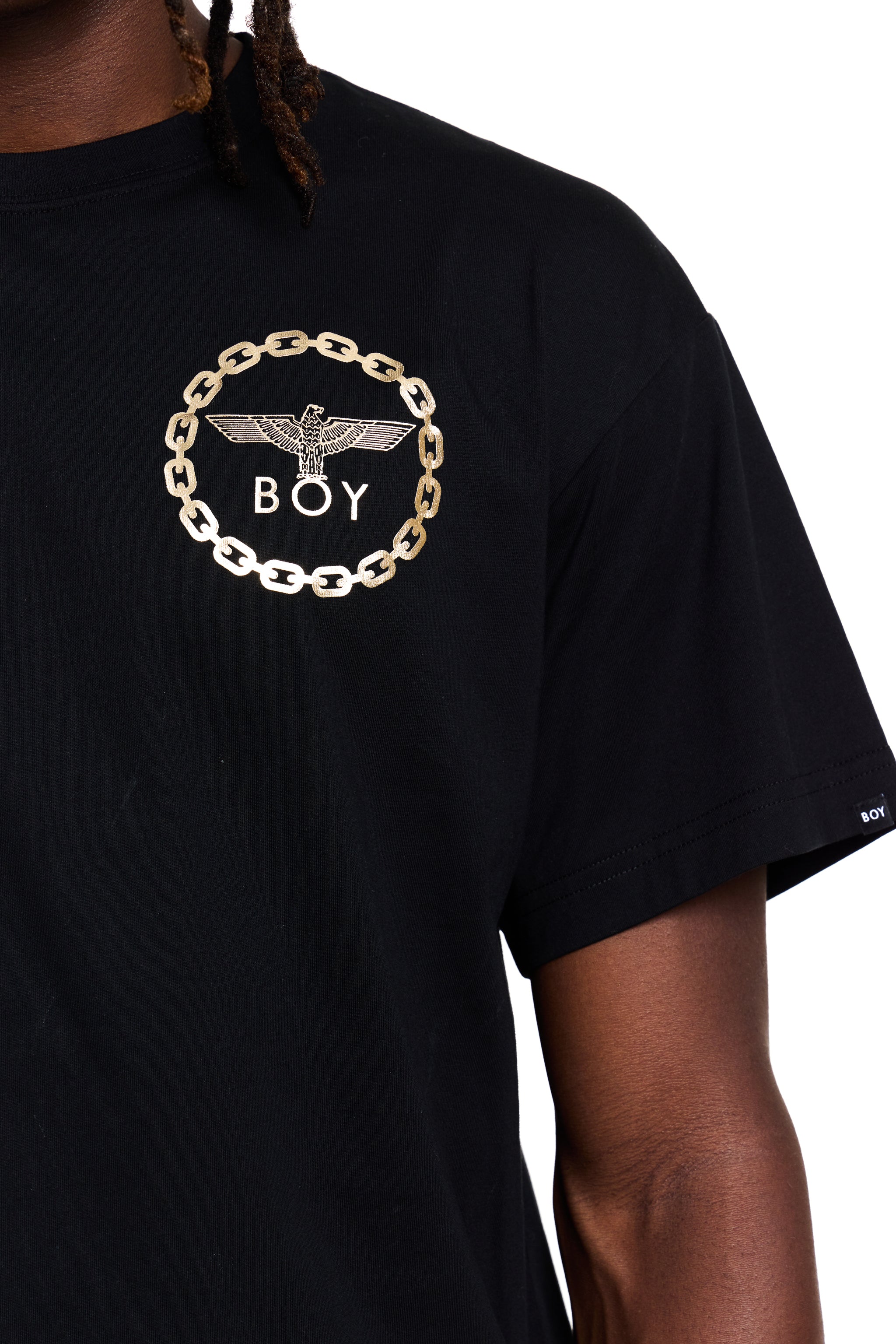 Black BOY London t-shirt with gold chain and eagle logo on a person wearing dreadlocks.
