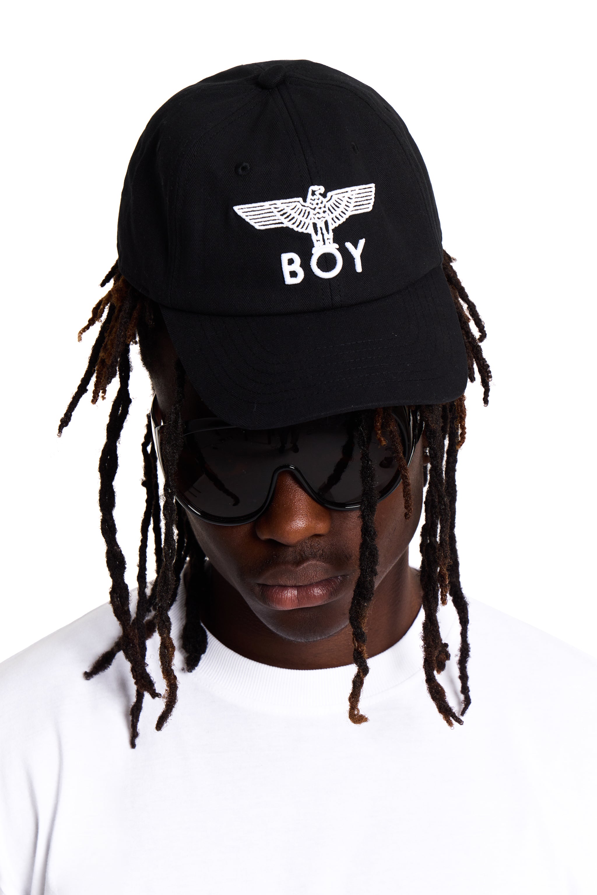 Person wearing a black cap with 'BOY' LONDON logo and sunglasses on a white background