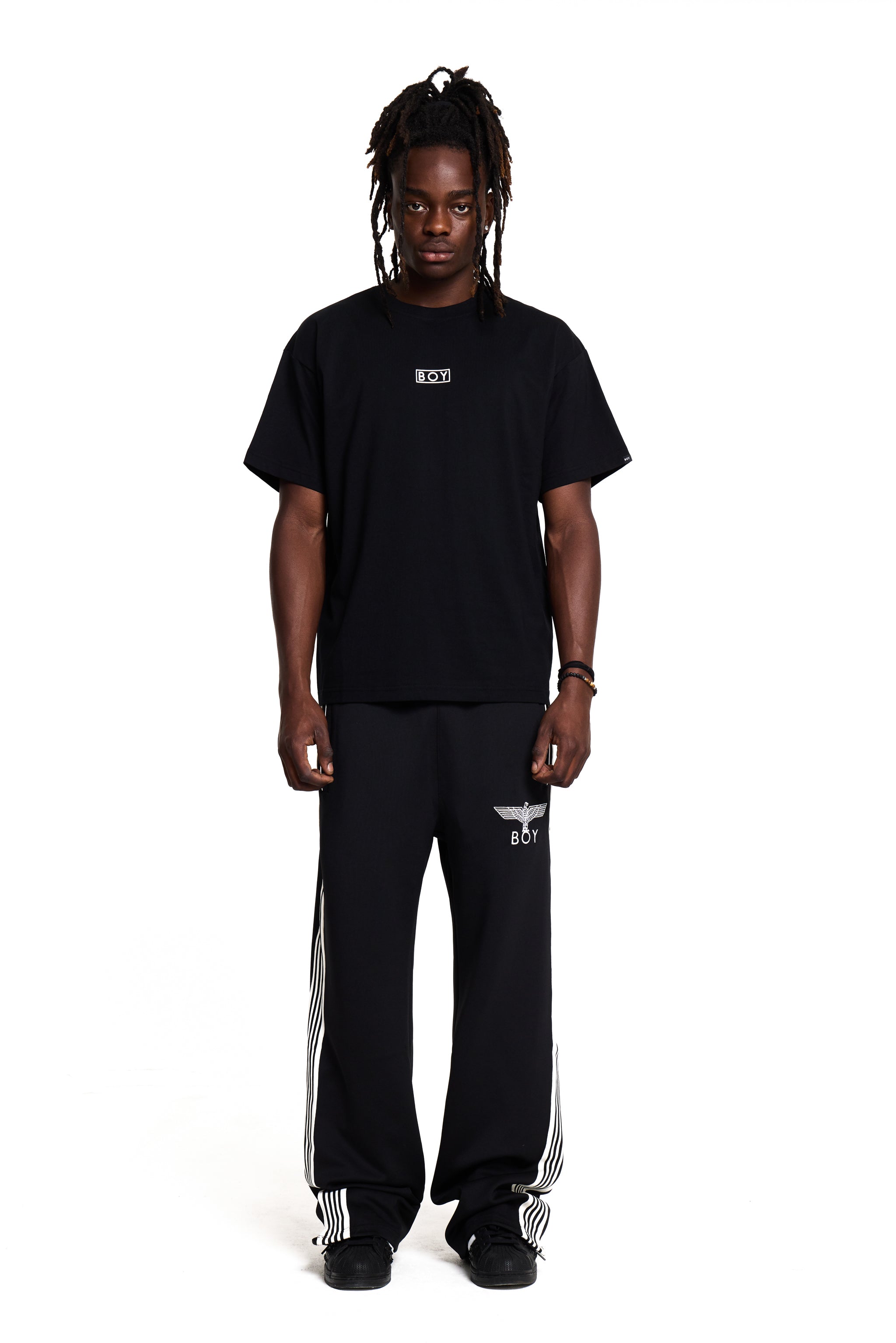 Model wearing a black BOY London t-shirt and black pants with white stripes on a white background 