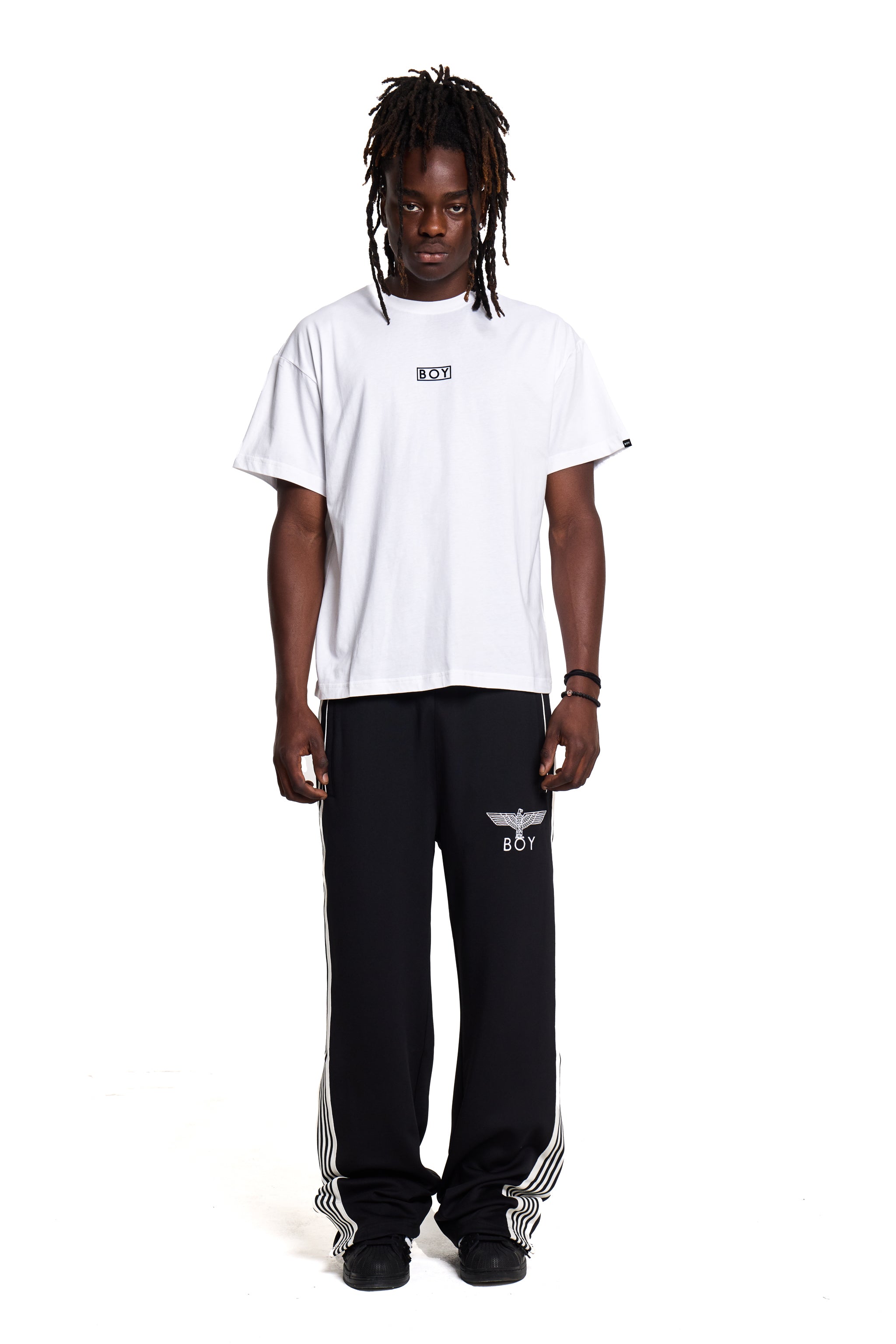 Model wearing a white BOY London  t-shirt and black pants with white stripes on a white background