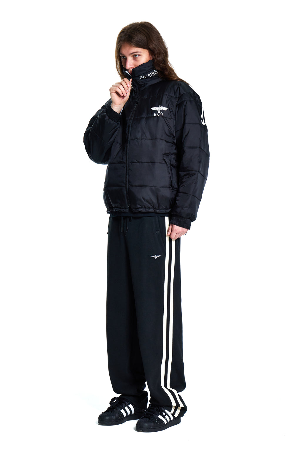 Person wearing a black puffer jacket and tracksuit with white stripes on a white background