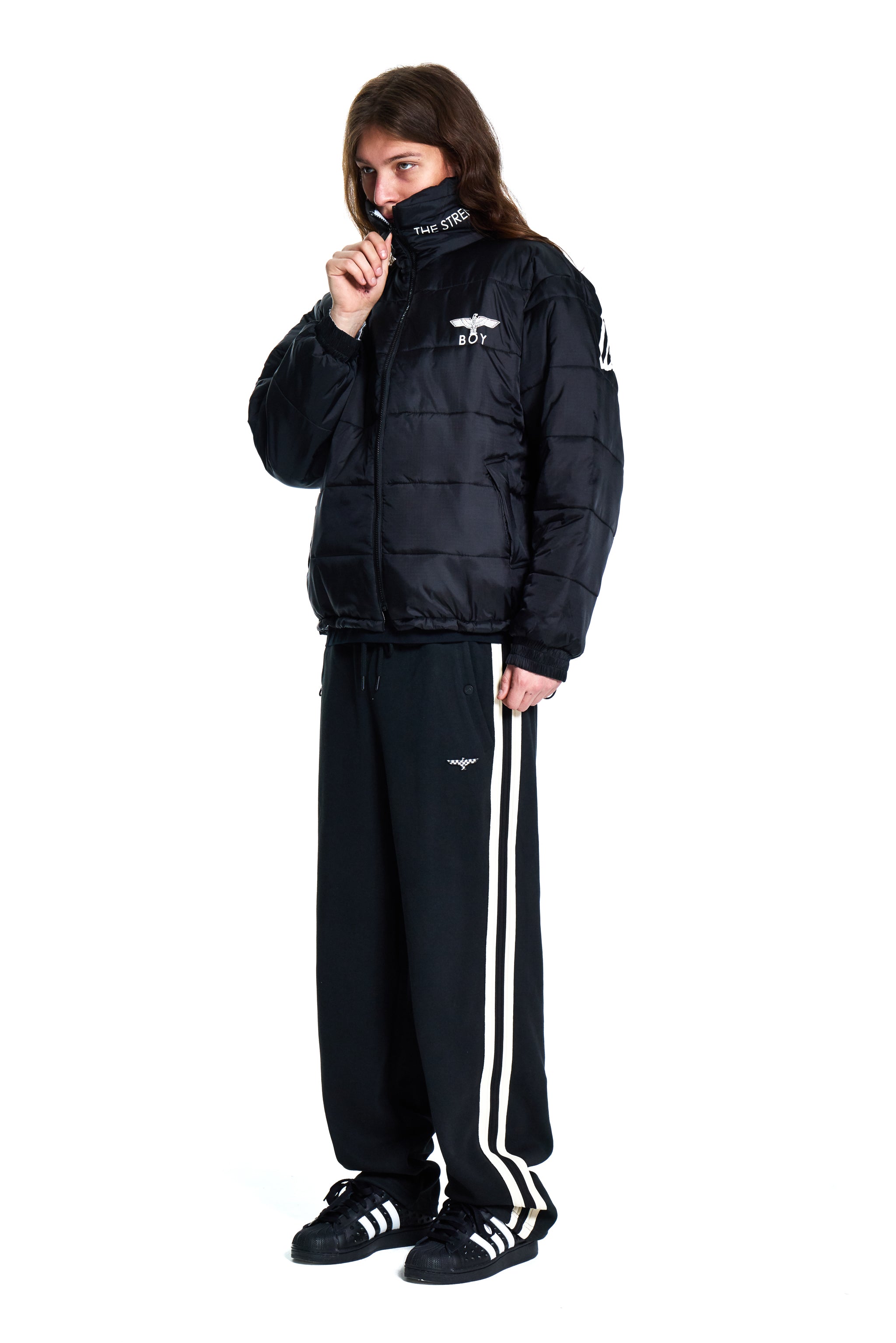 Person wearing a black puffer jacket and tracksuit with white stripes on a white background