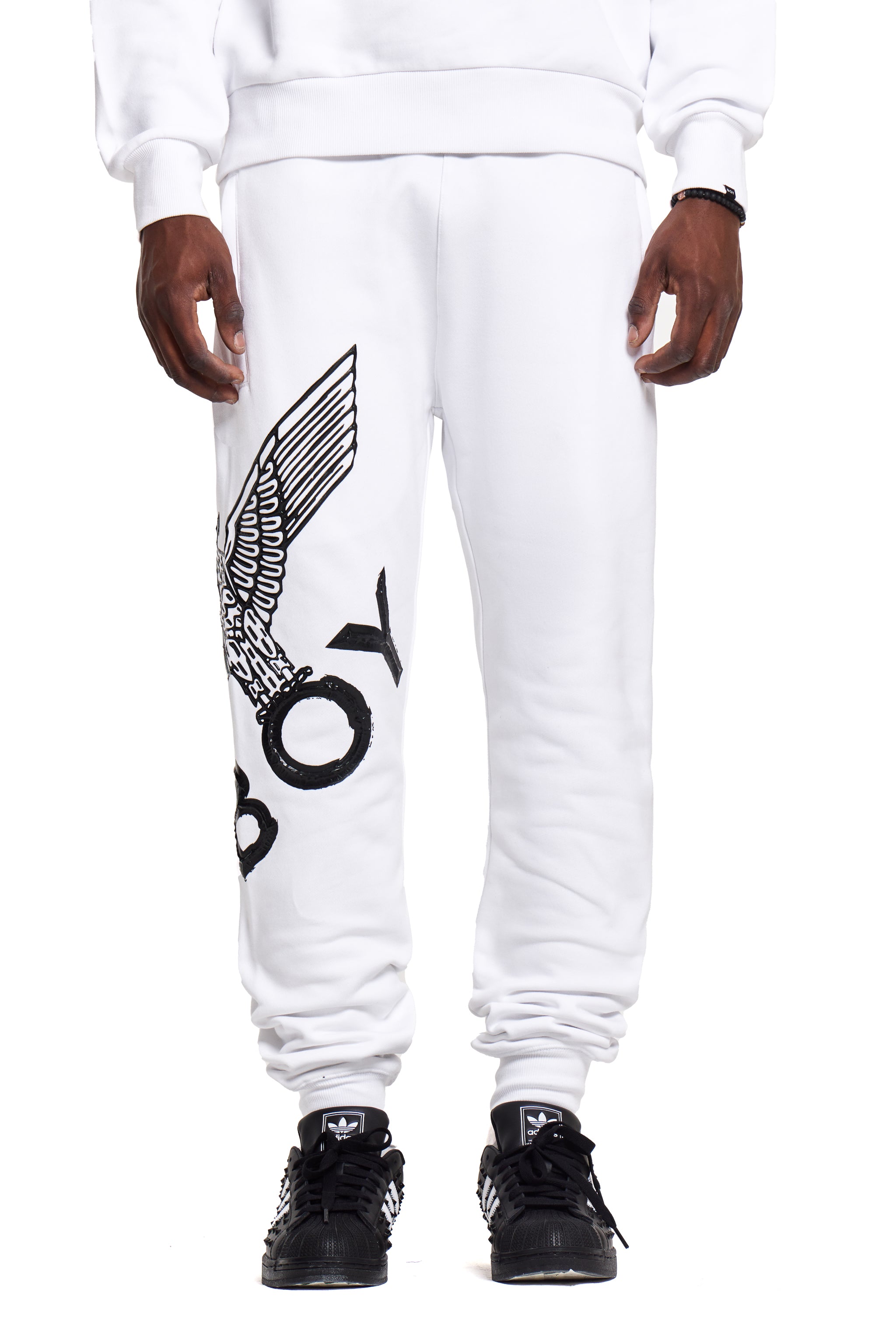White sweatpants with a BOY London logo and text design worn by a person on a white background