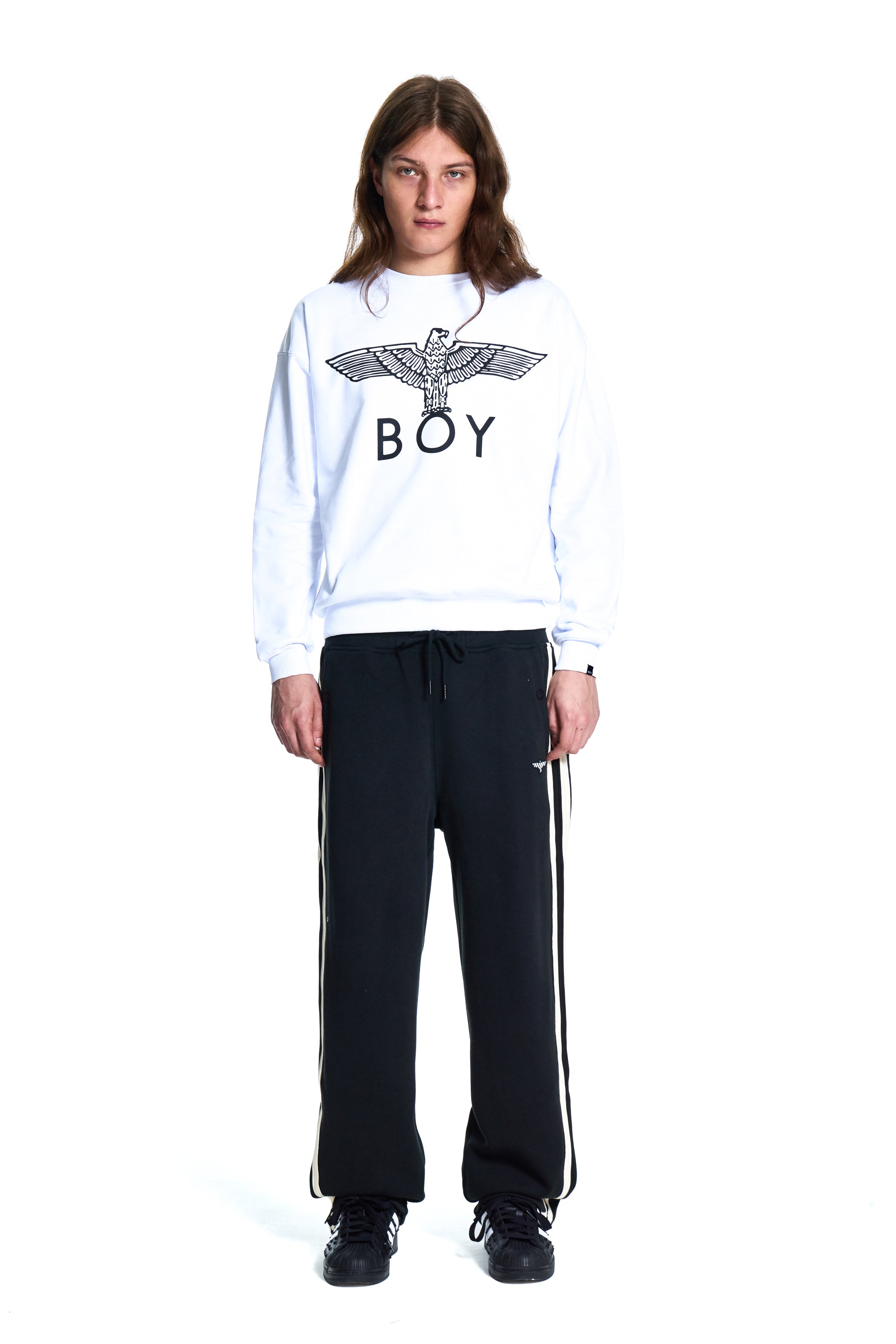 Person wearing a white sweatshirt with a logo and black pants on a white background