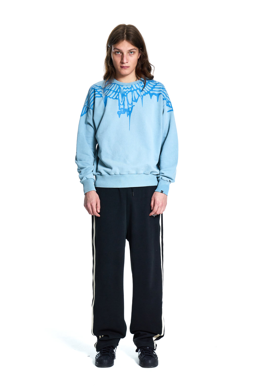 Person wearing a Boy London light blue sweater with a pattern and black pants on a white background