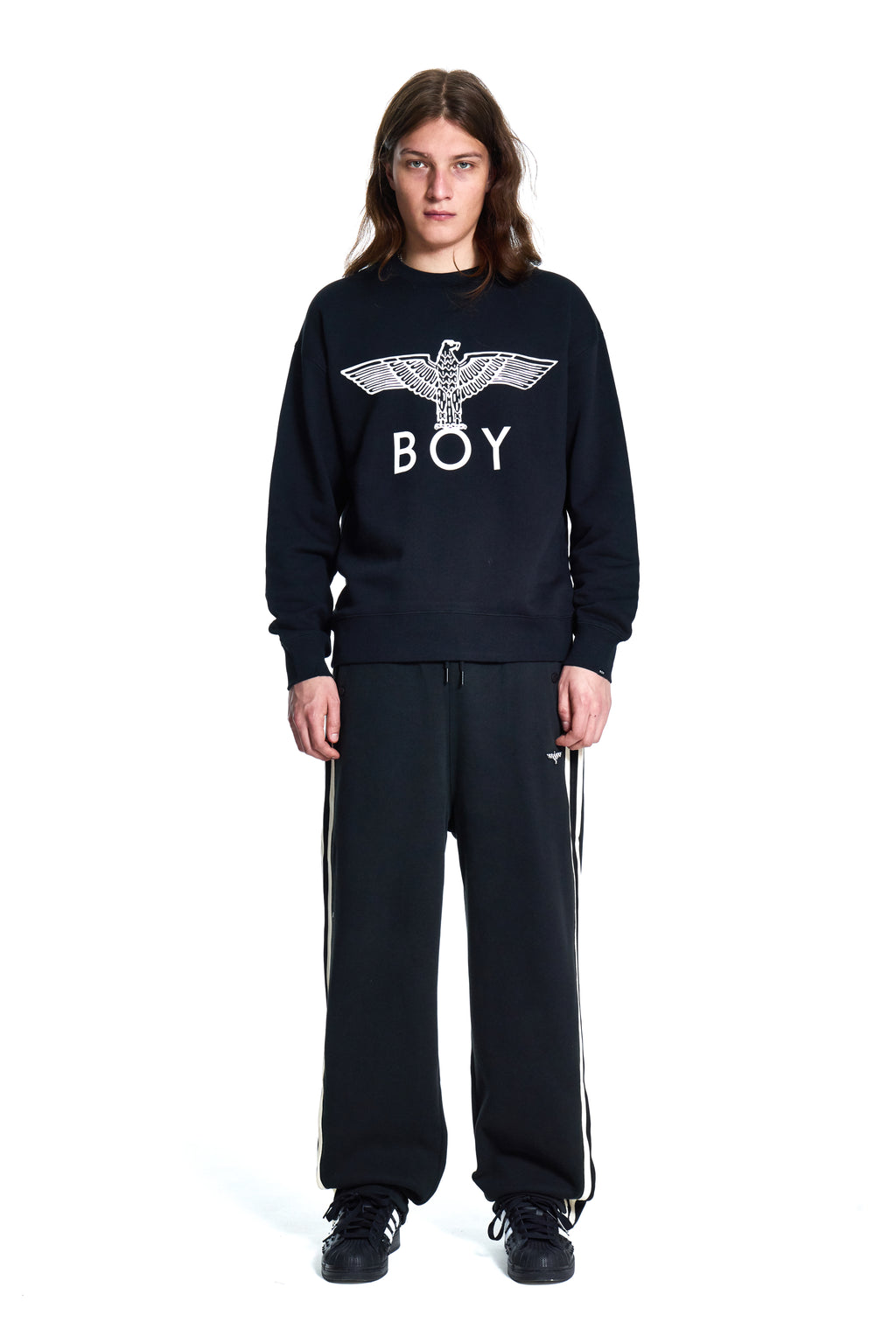 Person wearing a black sweatshirt with 'BOY' logo and black pants with white stripes on a white background