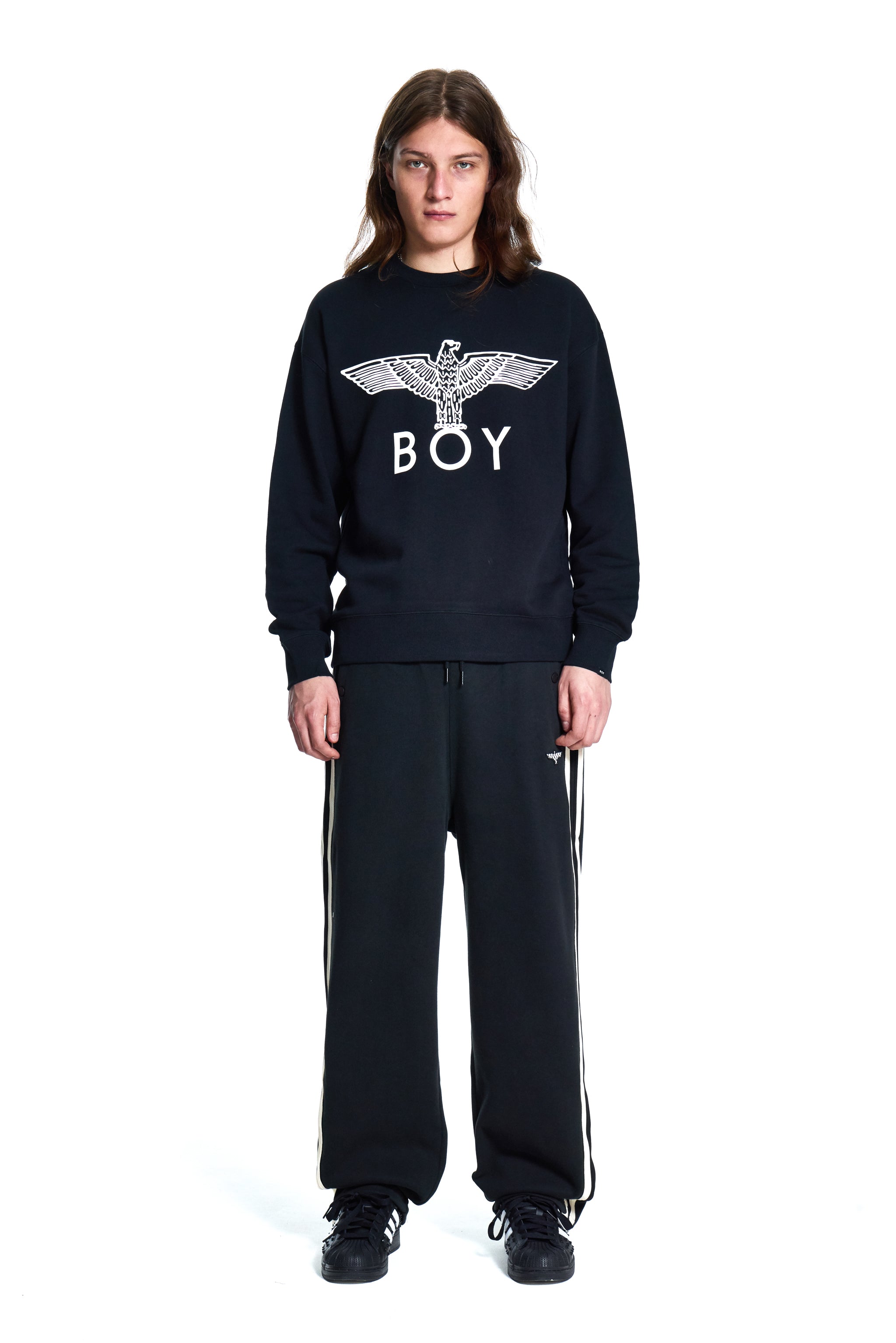 Person wearing a black sweatshirt with 'BOY' logo and black pants with white stripes on a white background