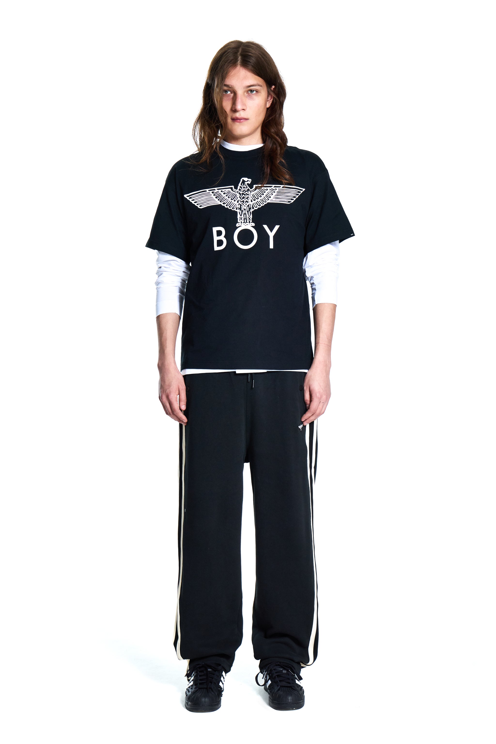 Person wearing a black Boy London t-shirt with 'BOY' logo and black pants with white stripes on a white background
