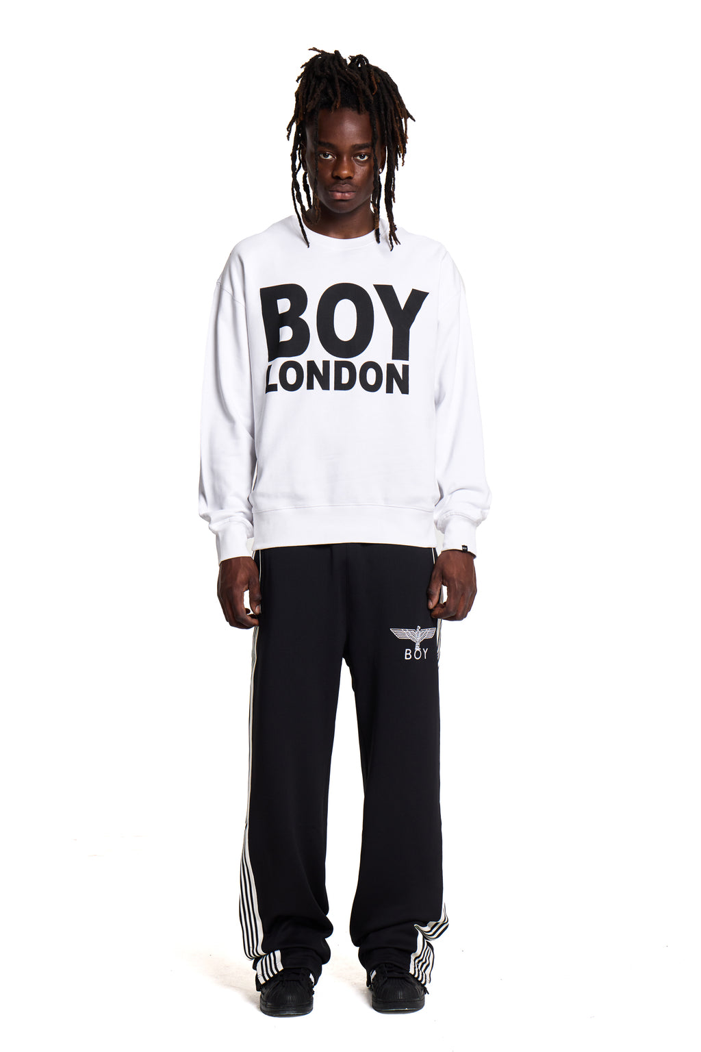 model wearing a white 'BOY LONDON' sweatshirt and black pants on a white background