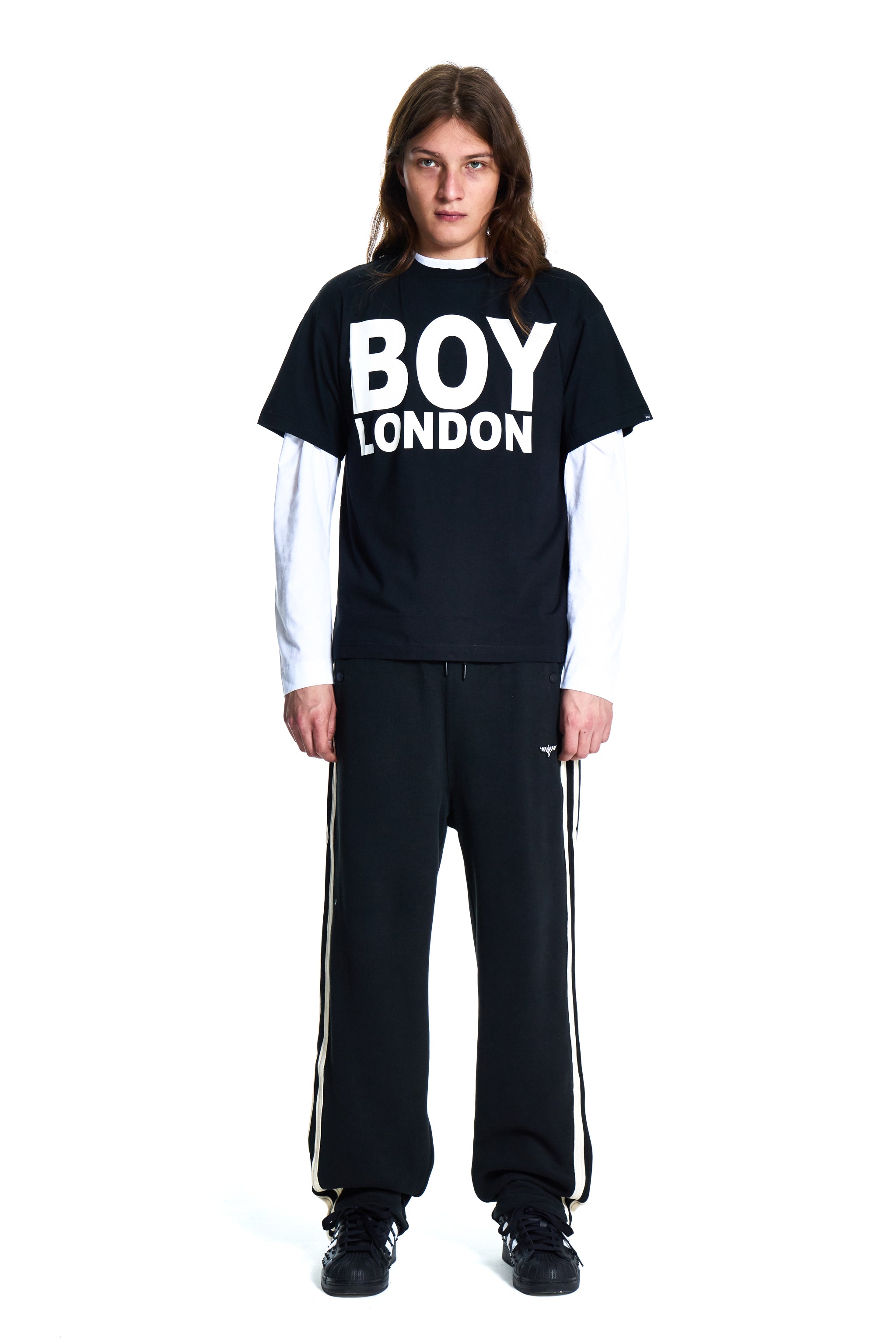 Person wearing a black 'BOY LONDON' t-shirt and black tracksuit with white stripes on a white background