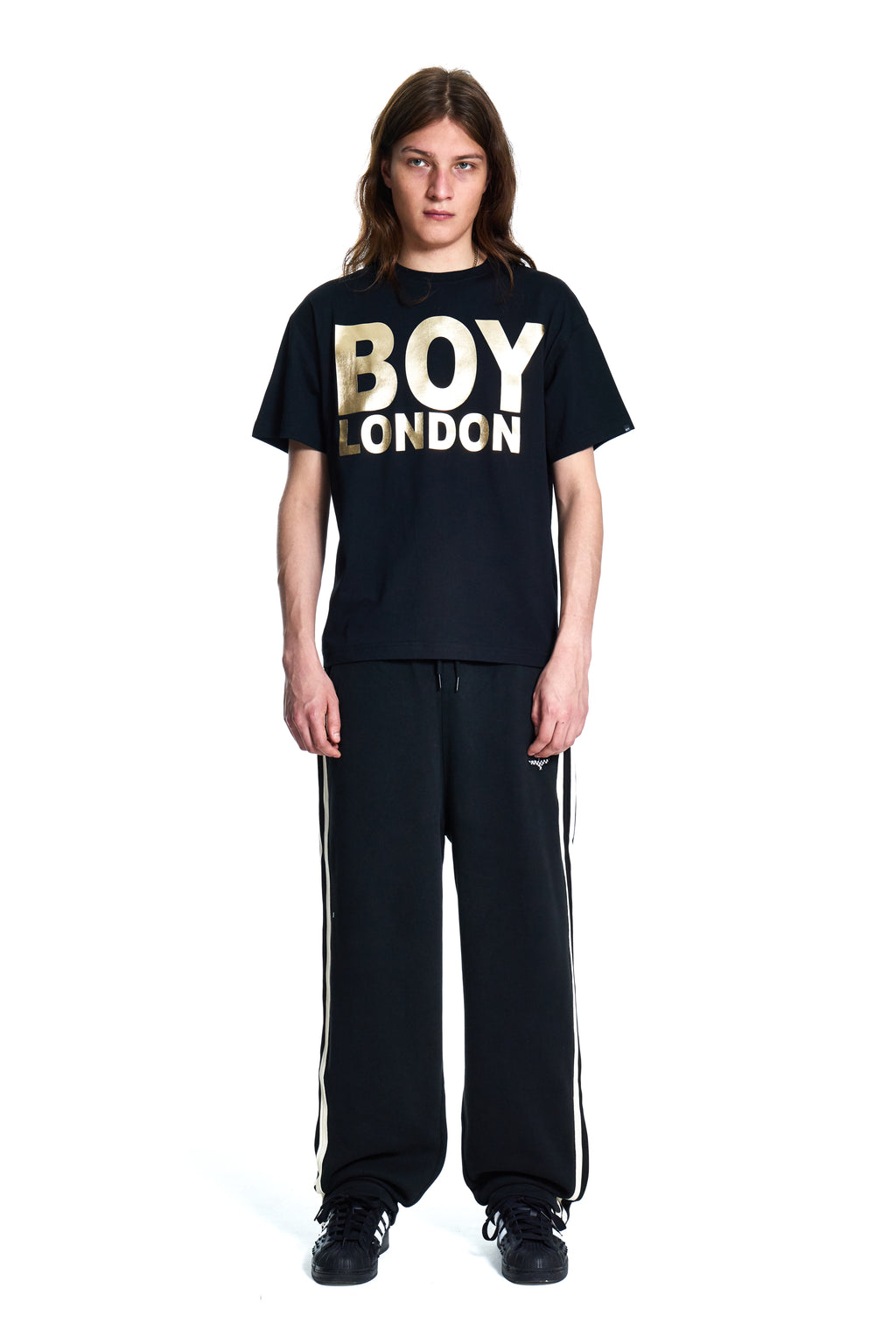 Person wearing a black 'BOY London' t-shirt and black pants with white stripes on a white background