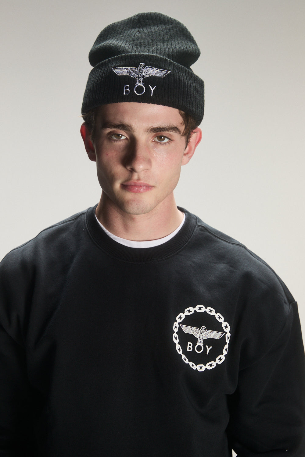 Person wearing a black beanie and sweatshirt with 'BOY' London  logo on a plain background