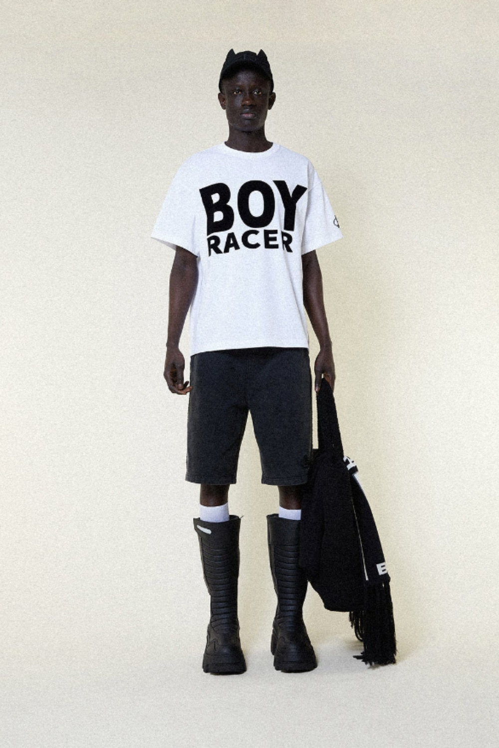 Person wearing a BOY LONDON white t-shirt with 'BOY RACER' text, black shorts, and black boots on a plain background