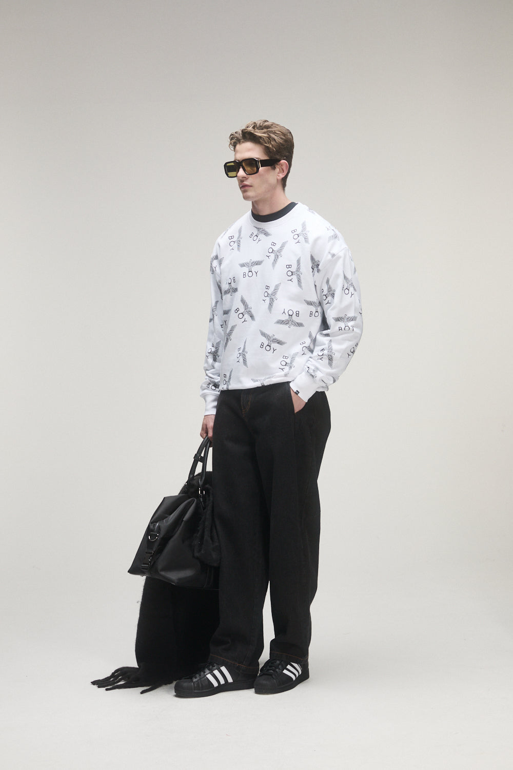 Person wearing a Boy London white patterned sweatshirt, black pants, and black shoes on a gray background