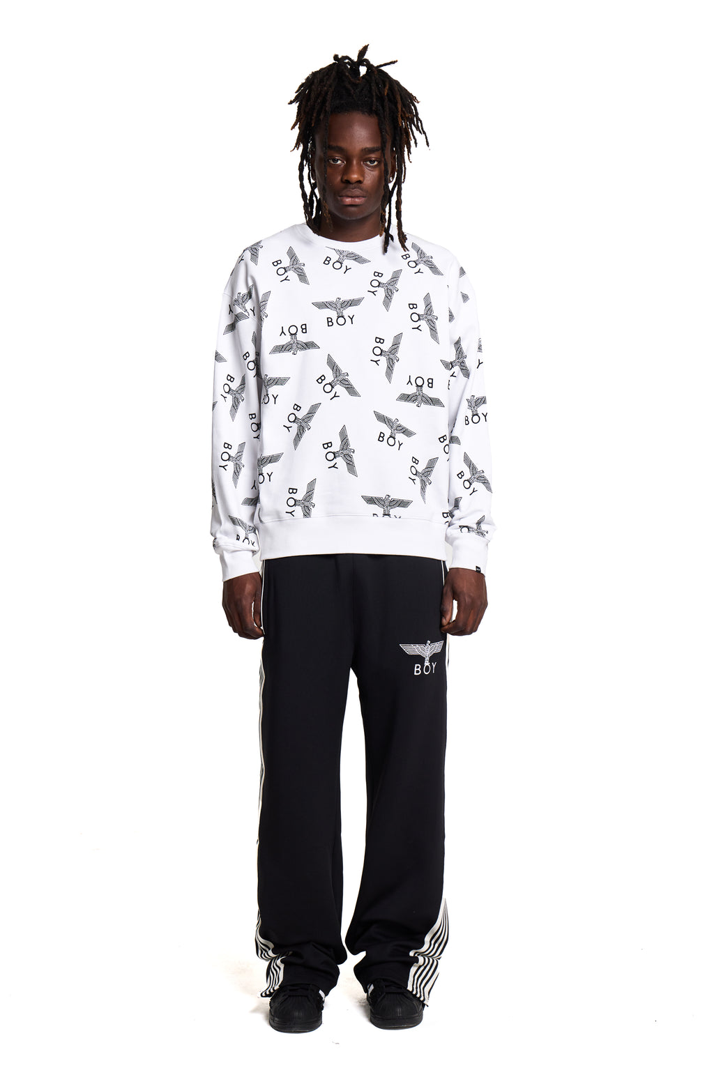 Person wearing a white Boy London sweatshirt with airplane pattern and black pants on a white background