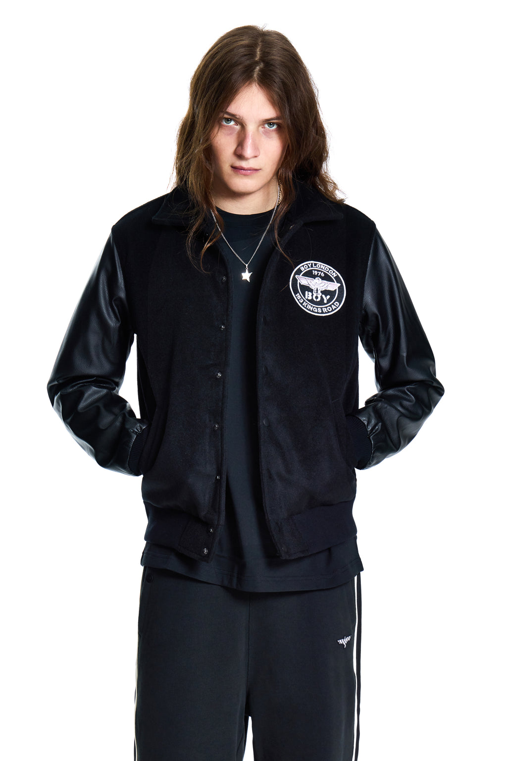 Person wearing a black jacket with a logo and dark pants on a white background