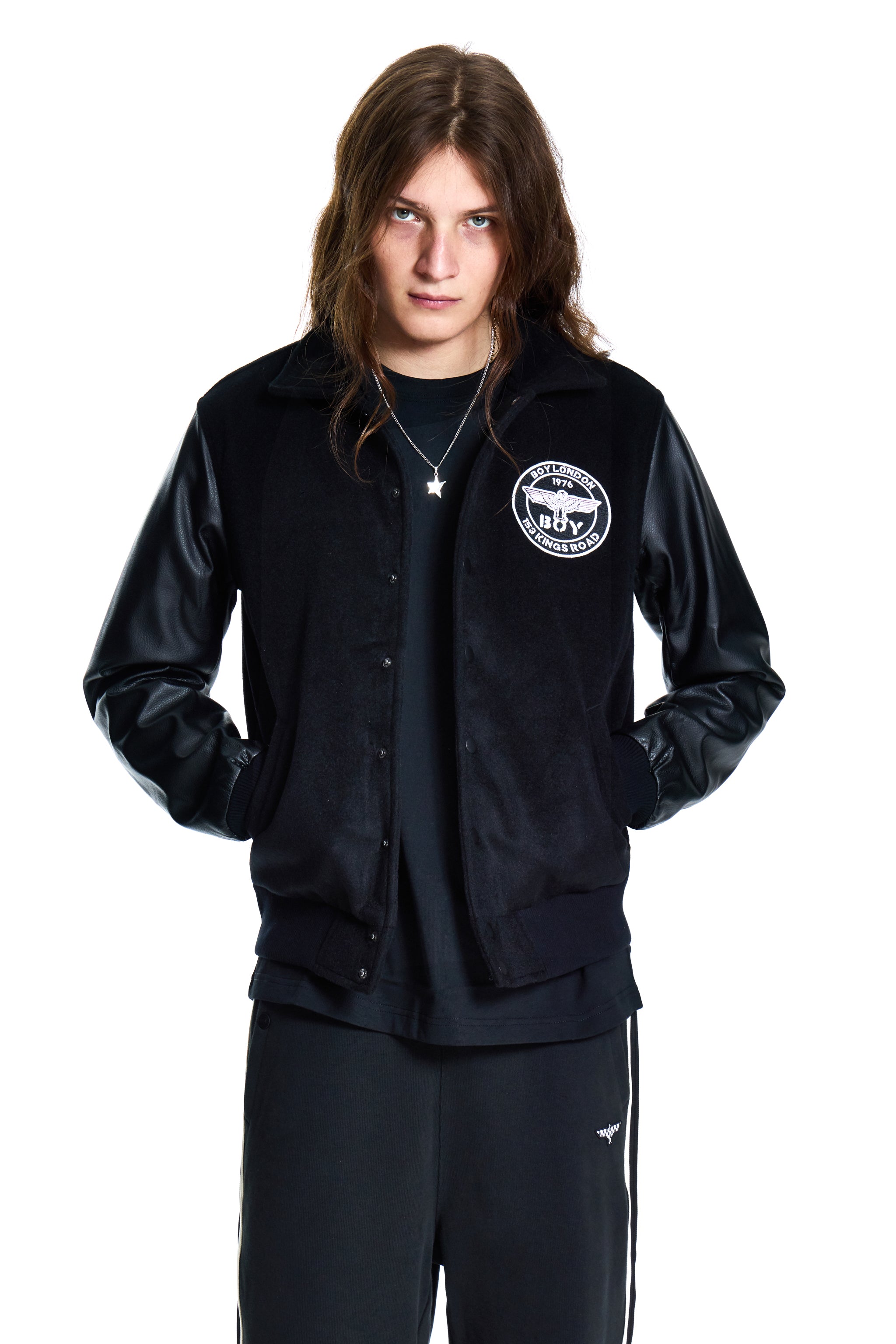 Person wearing a black jacket with a logo and dark pants on a white background