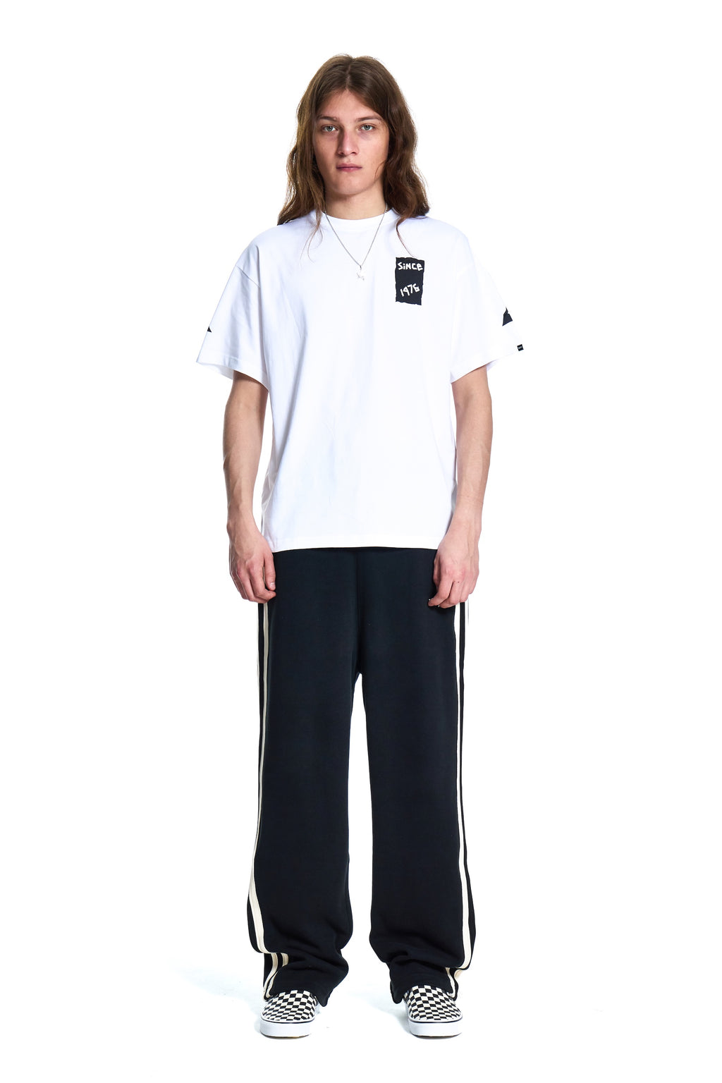 Person wearing a white Boy London t-shirt with a logo and black pants with white stripes on a white background