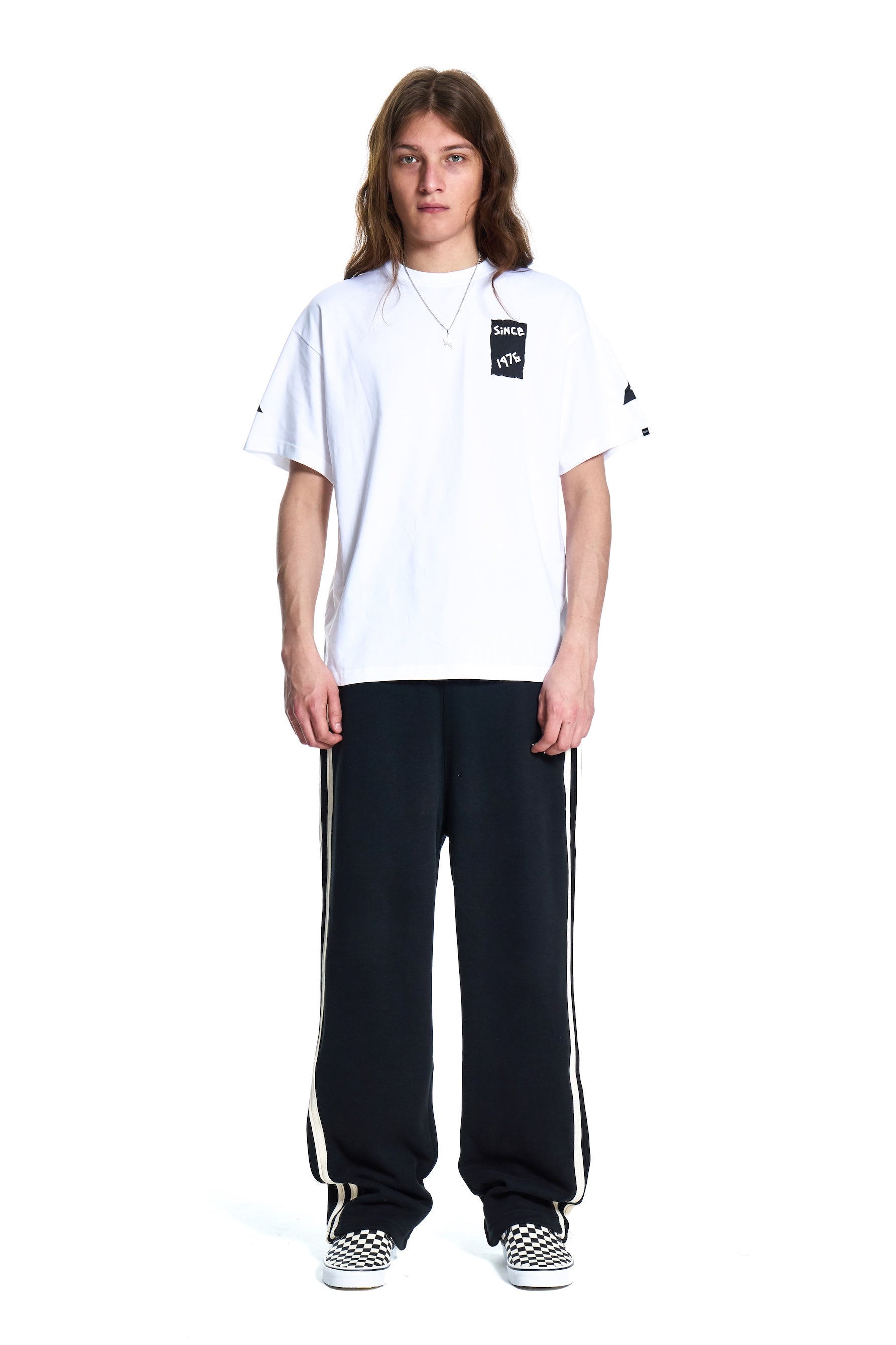 Person wearing a white Boy London t-shirt with a logo and black pants with white stripes on a white background