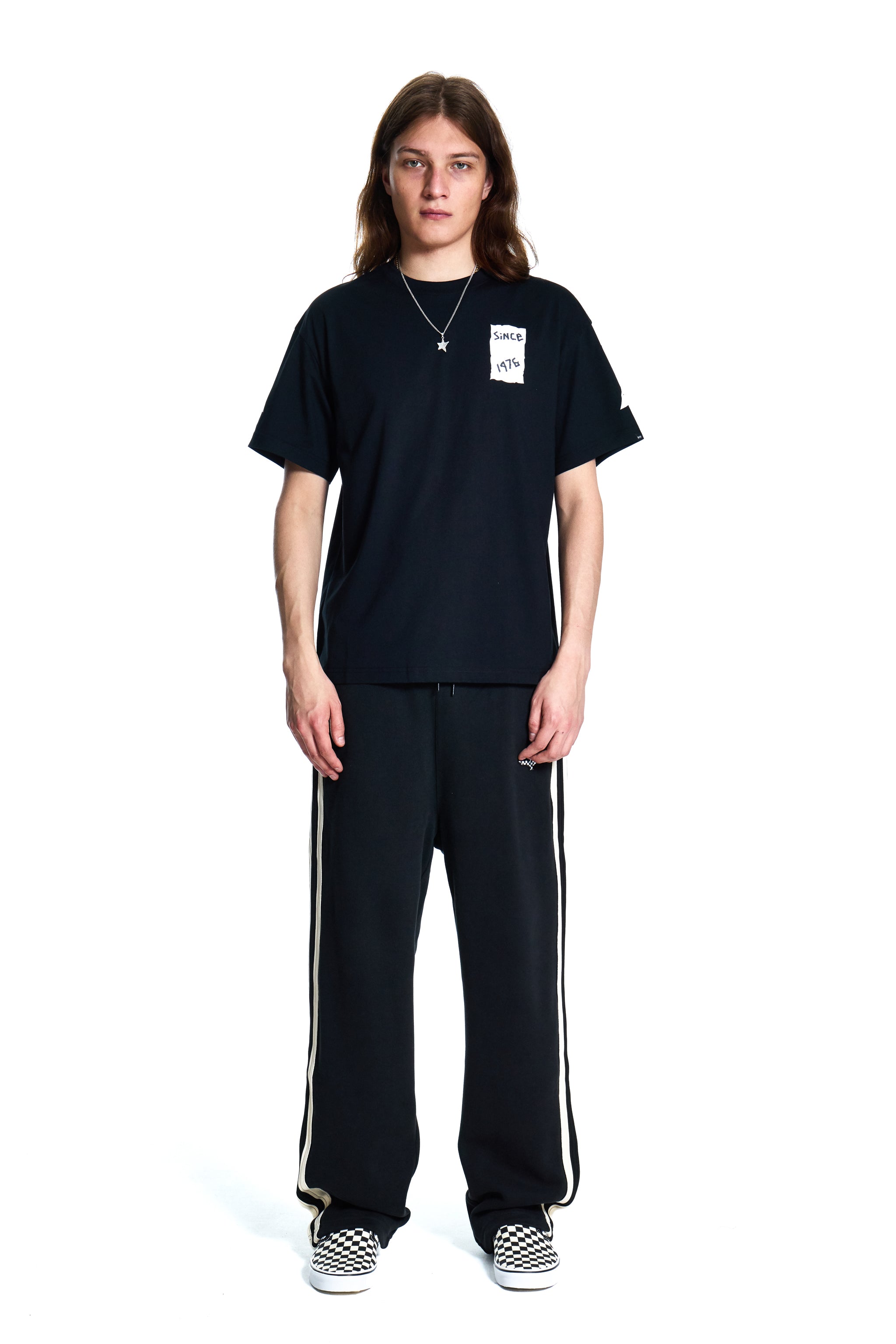 Person wearing a black Boy London t-shirt and black pants with white stripes on a white background