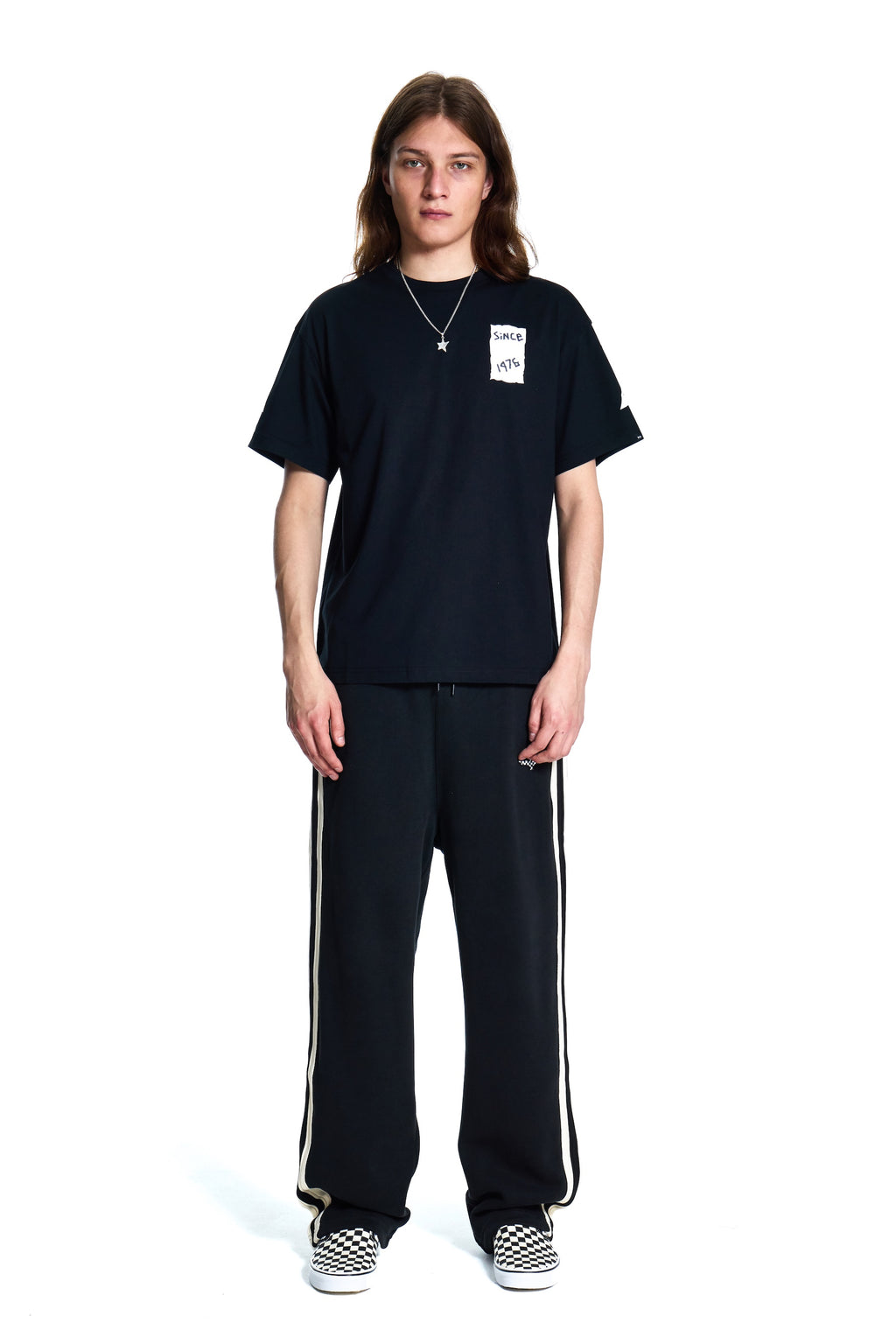 Person wearing a black t-shirt and black pants with white stripes on a white background