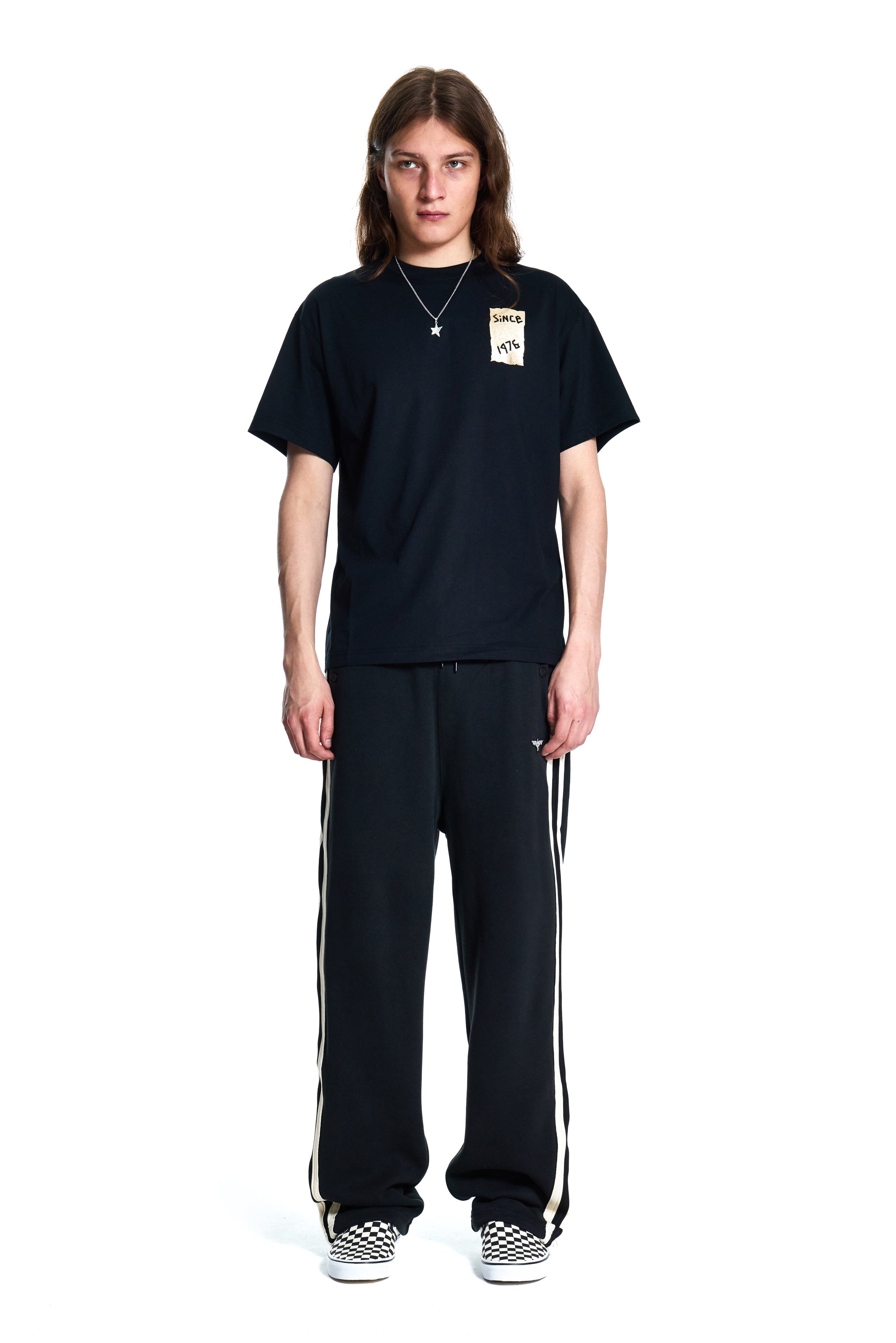Person wearing a black t-shirt and black pants with white stripes on a white background