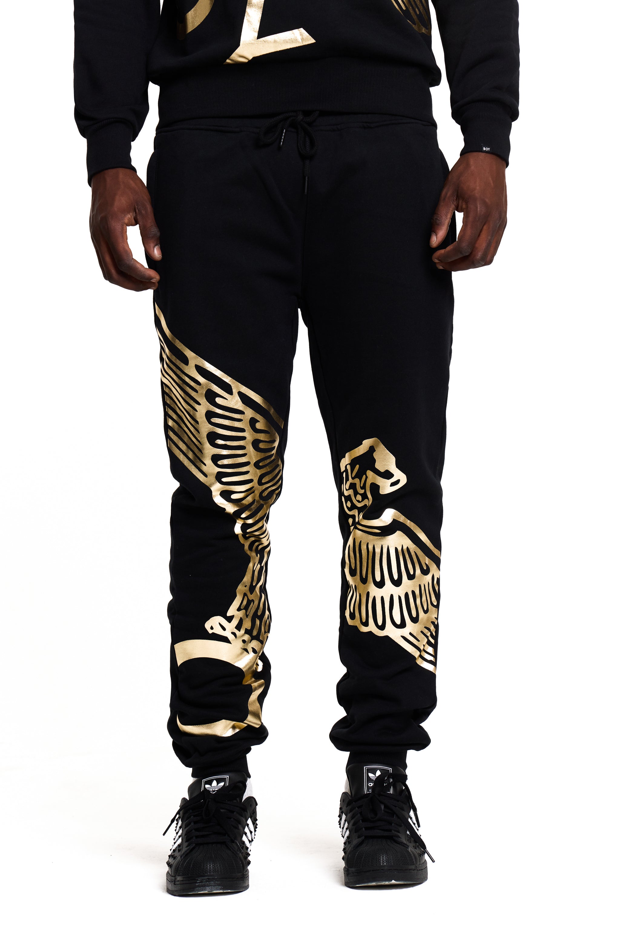 Black BOY London jogger pants with gold skeleton design worn by a person on a white background