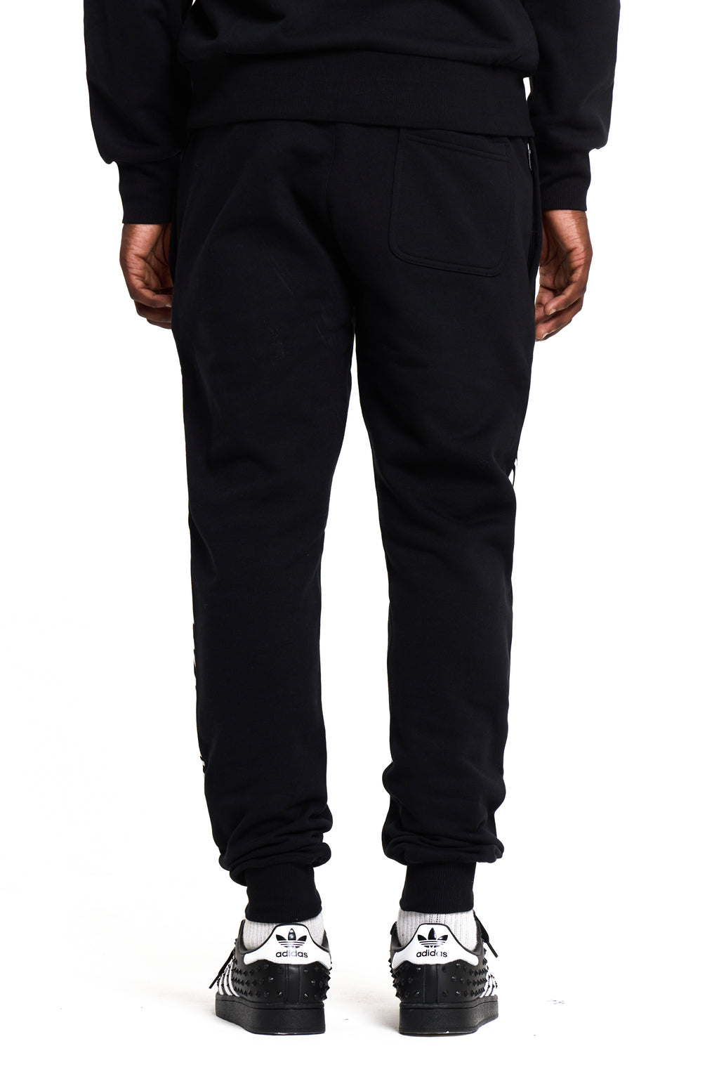 Person wearing black BOY London sweatpants with white sneakers on a white background
