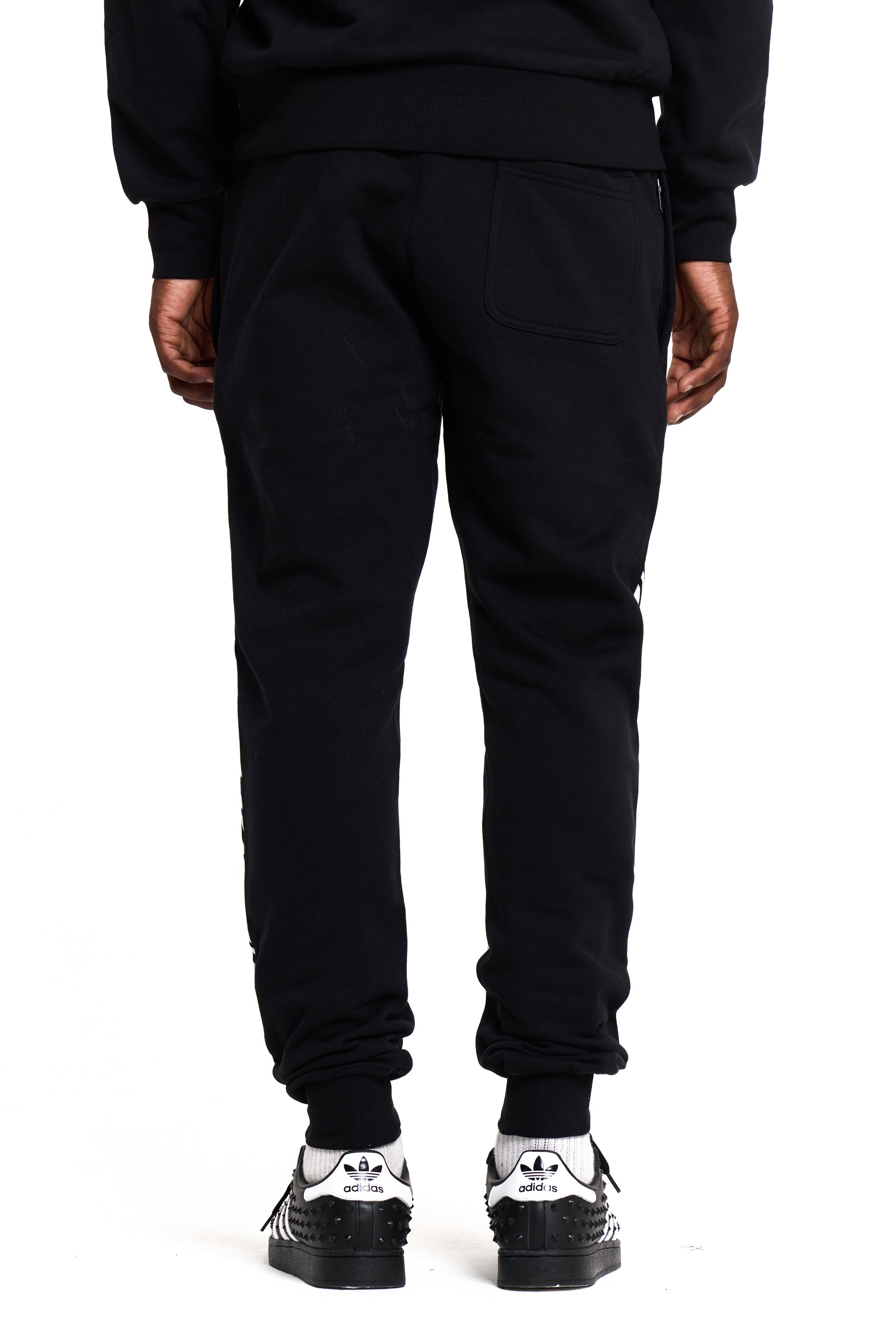 Person wearing black BOY London sweatpants with white sneakers on a white background